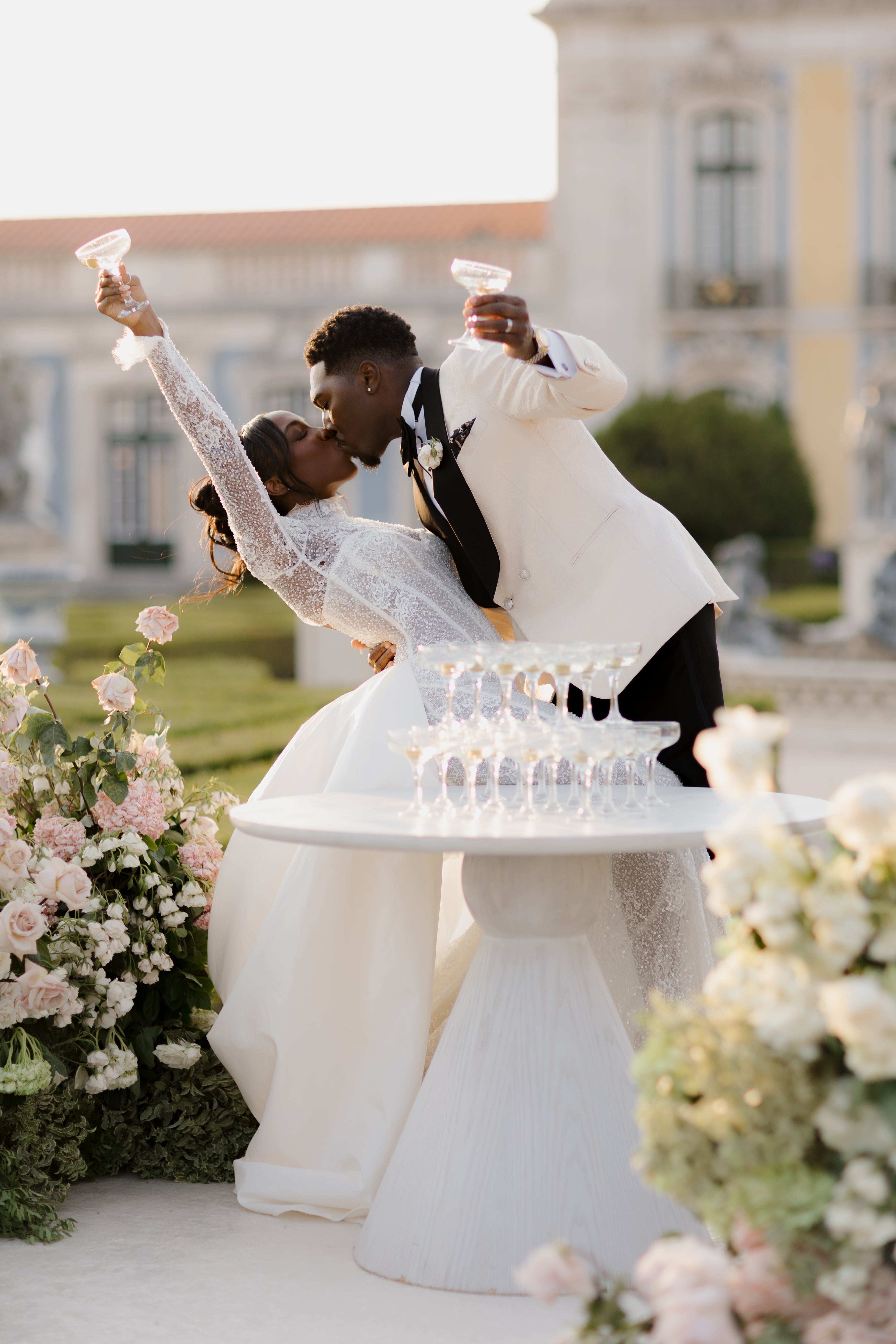 Couple in wedding attire celebrating with champagne flutes in front of a classical building.