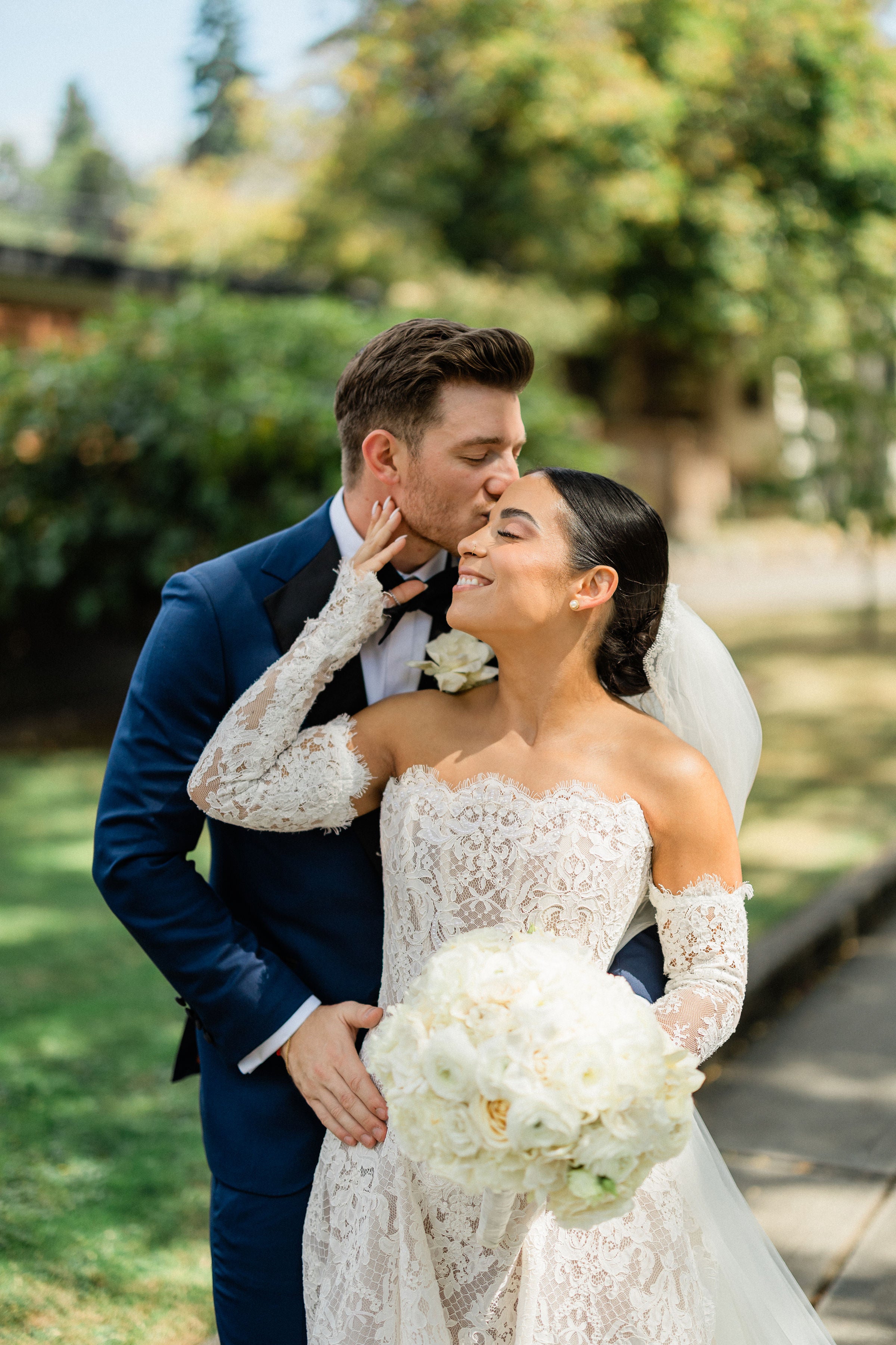 GL Bride Megan in Galia Lahav's Splendid couture wedding gown, being kissed on the cheek by groom with a blurred outdoor background