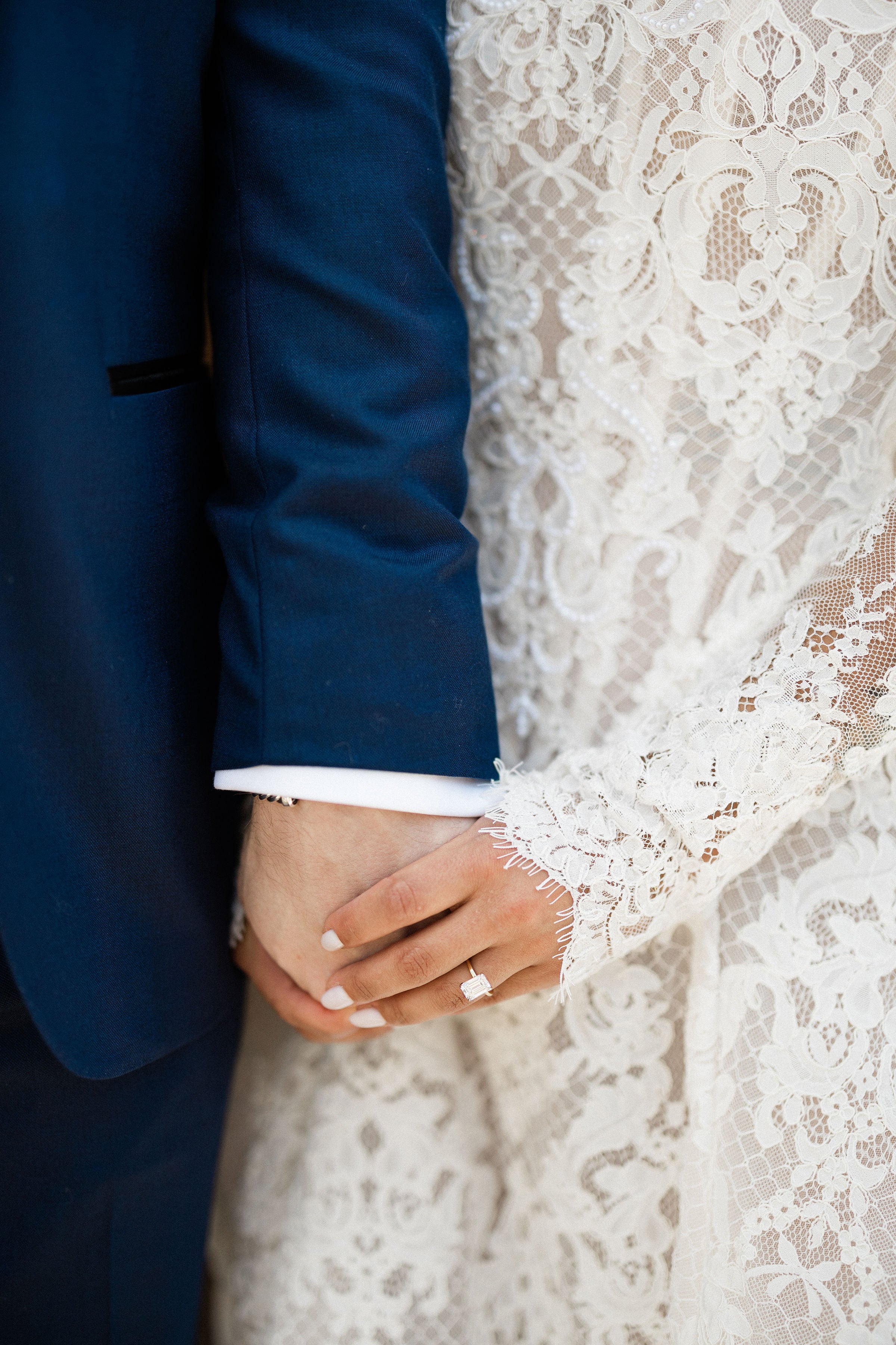 Close-up of hands holding each other with a focus on a ring, wearing formal attire.