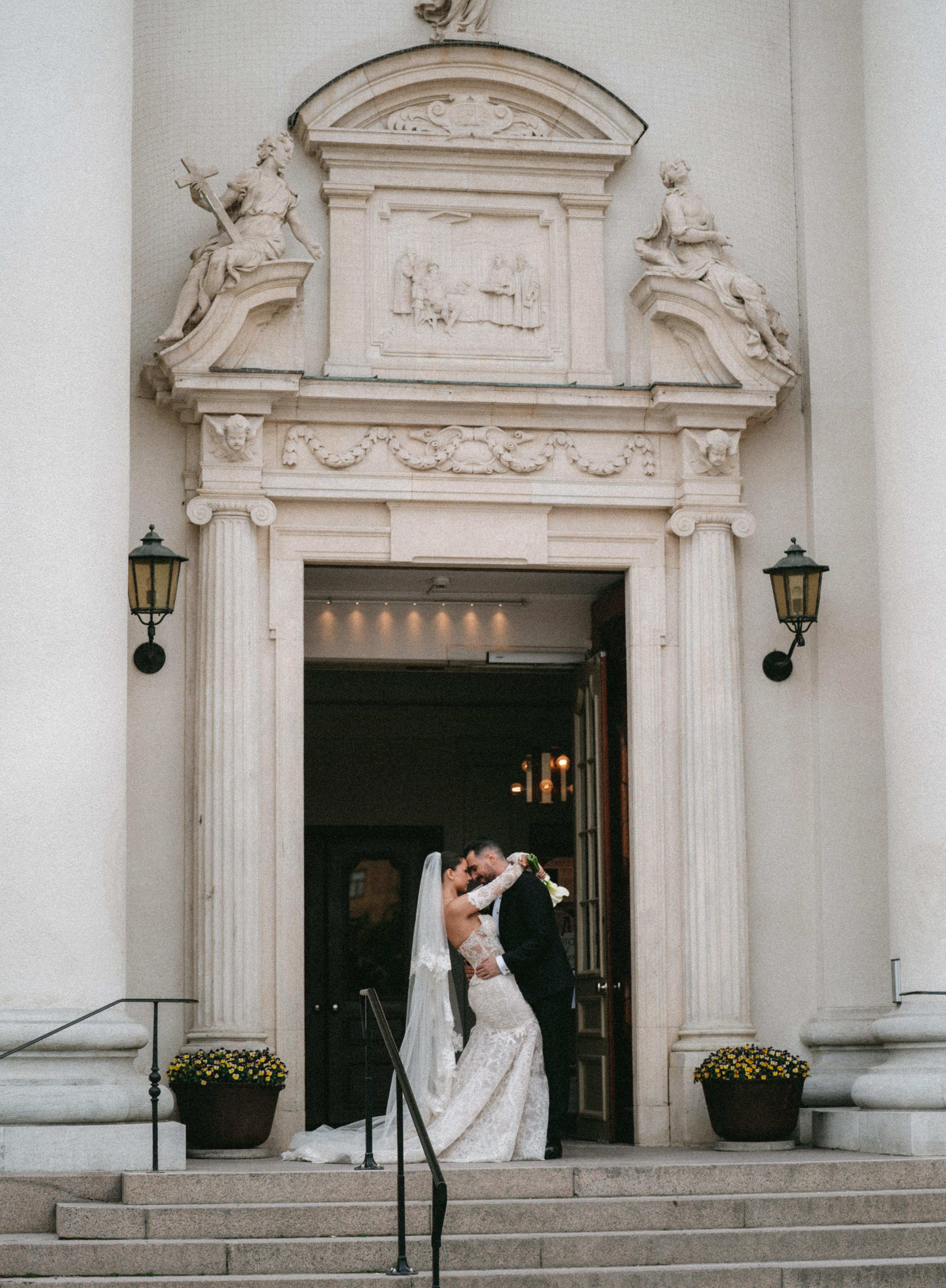 GL Bride Rebecca in our Scarlett gown with her groom embracing in front of an ornate building entrance.