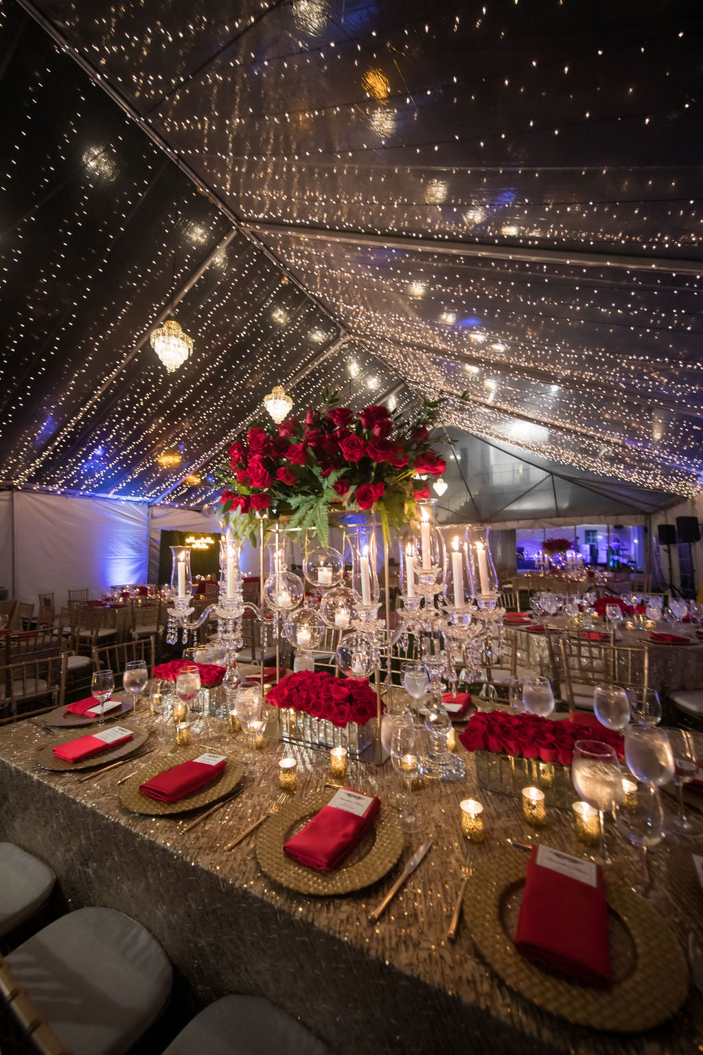 wedding reception decor with shimmering string lights, golden table tops and red rose arrangements 