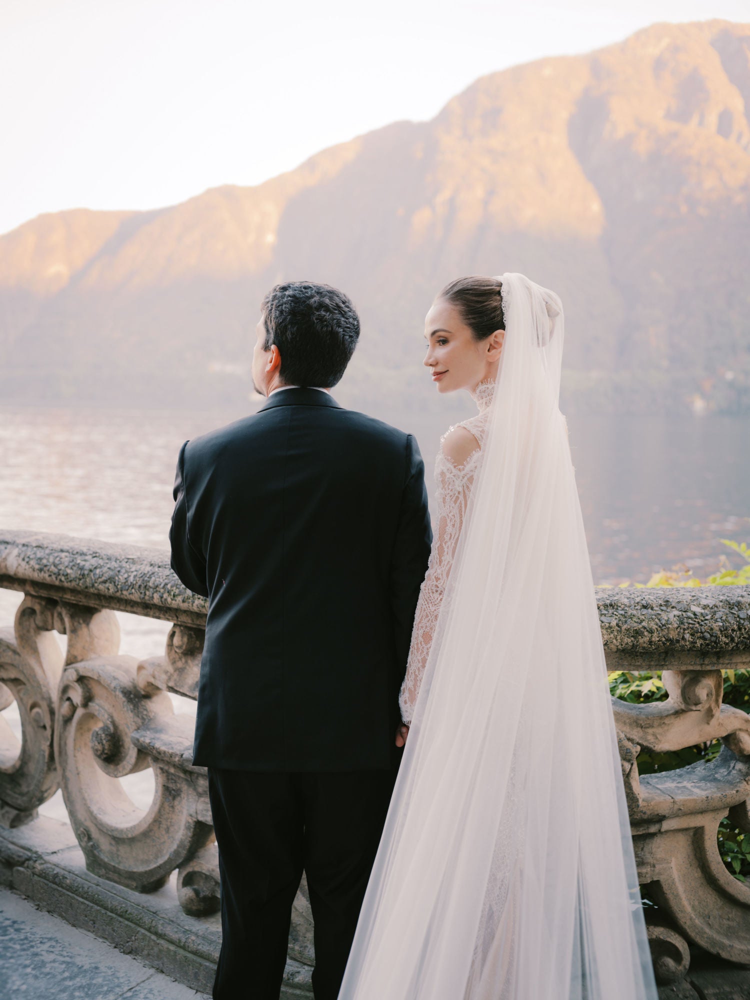 GL Bride Sarah Ingle in Élysée with her groom standing on a balcony with mountains in the background