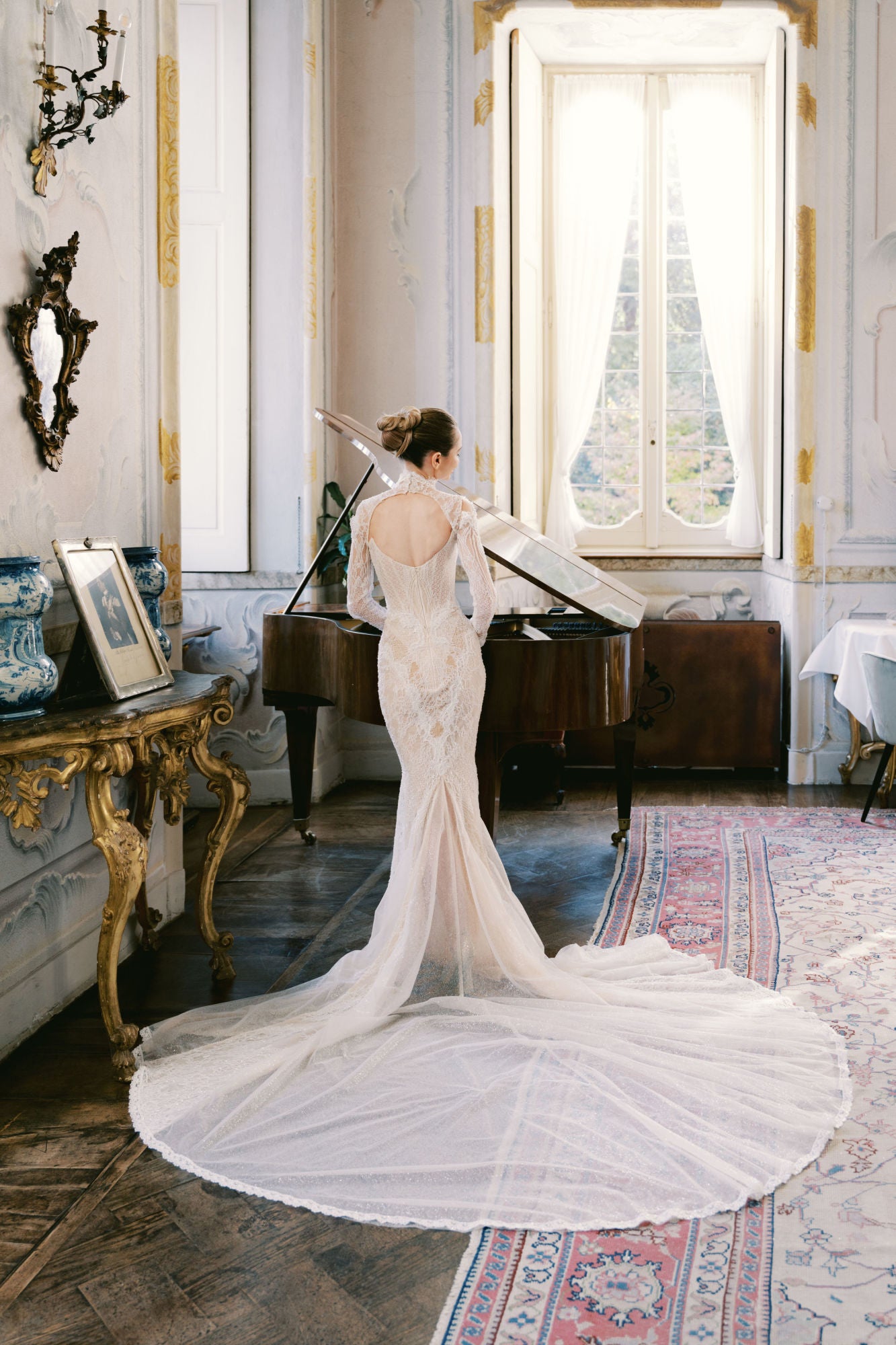 GL Bride Sarah Ingle in Galia Lahav's Élysée standing in a room with a grand piano and decorative elements.
