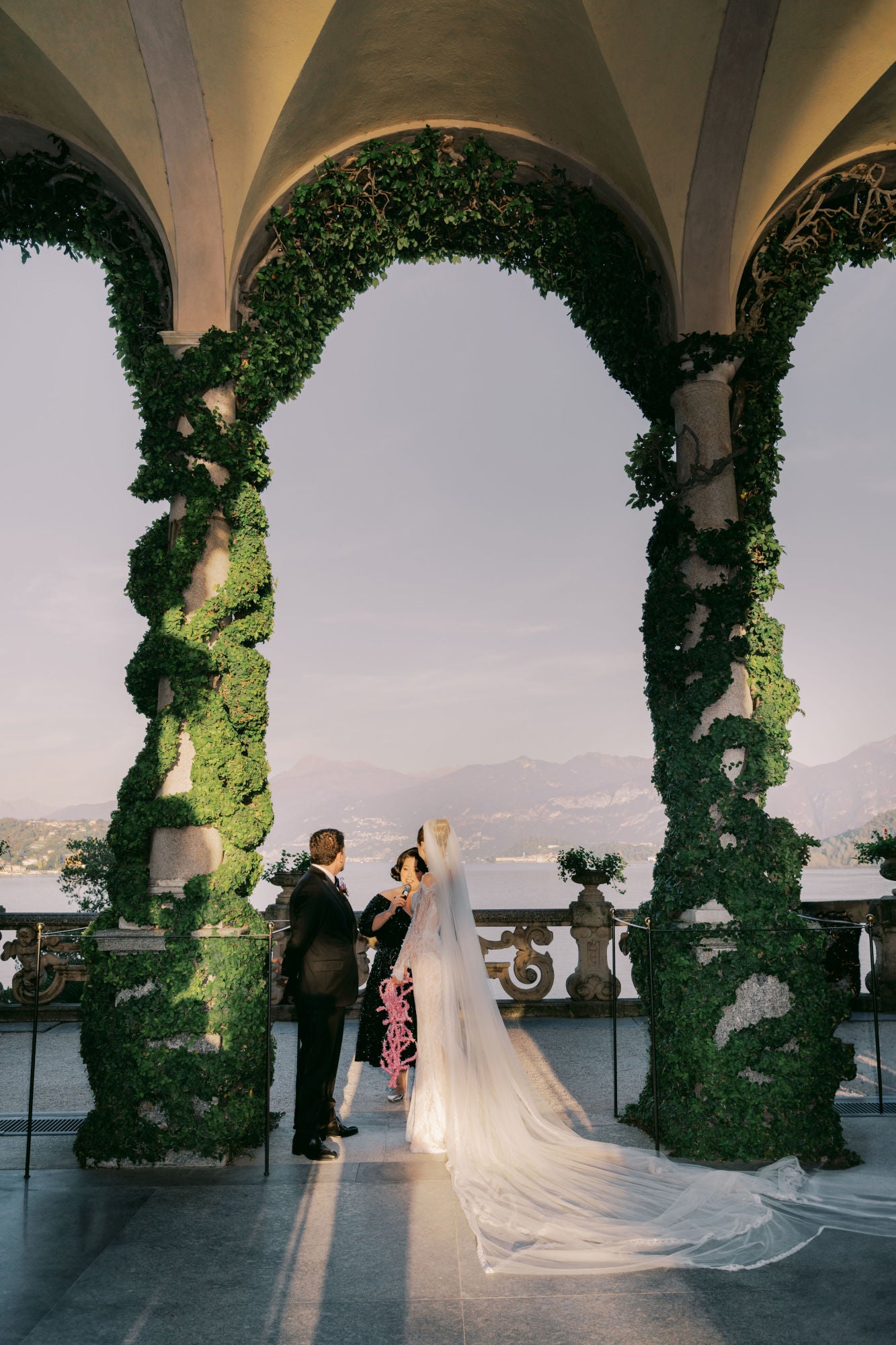 GL Bride Sarah in our Élysée standing with her groom under a decorative archway with greenery