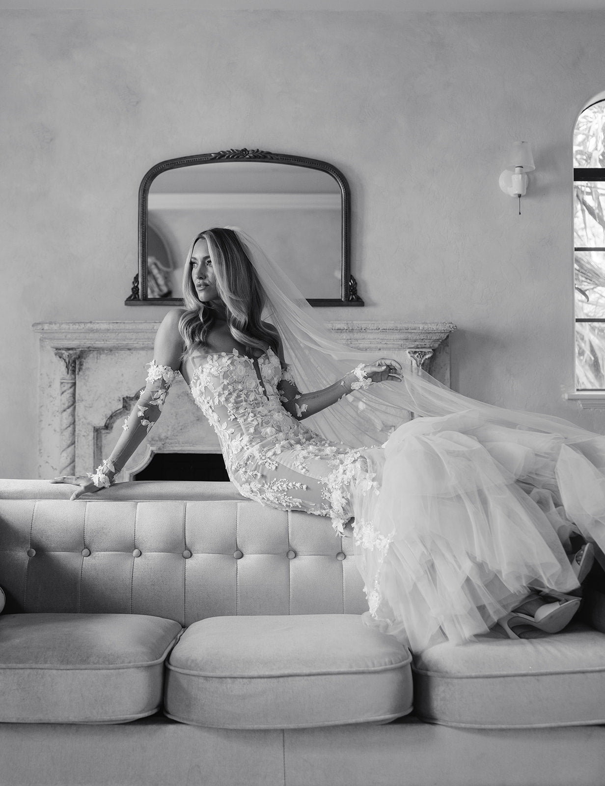 GL Bride Summer Fox in a Veronica wedding dress sitting on a couch with a veil draped over her head.