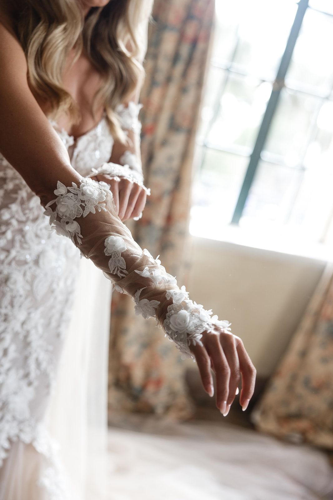 Close-up of Summer Fox wearing a lace wedding glove with floral details, blurred background. 