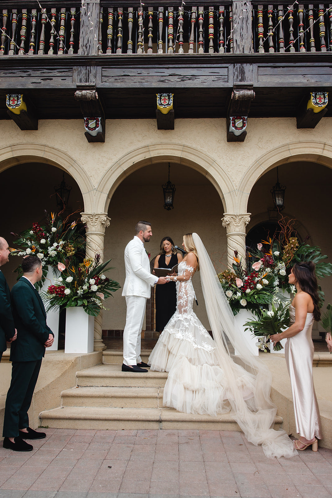 Wedding ceremony taking place in an elegant outdoor setting with arches and floral decorations.