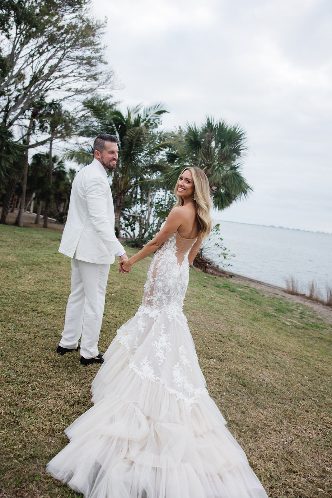 Summer Fox and husband standing on grass with a body of water and trees in the background. GL Bride Summer Fox wearing the Galia Lahav Veronica Gown