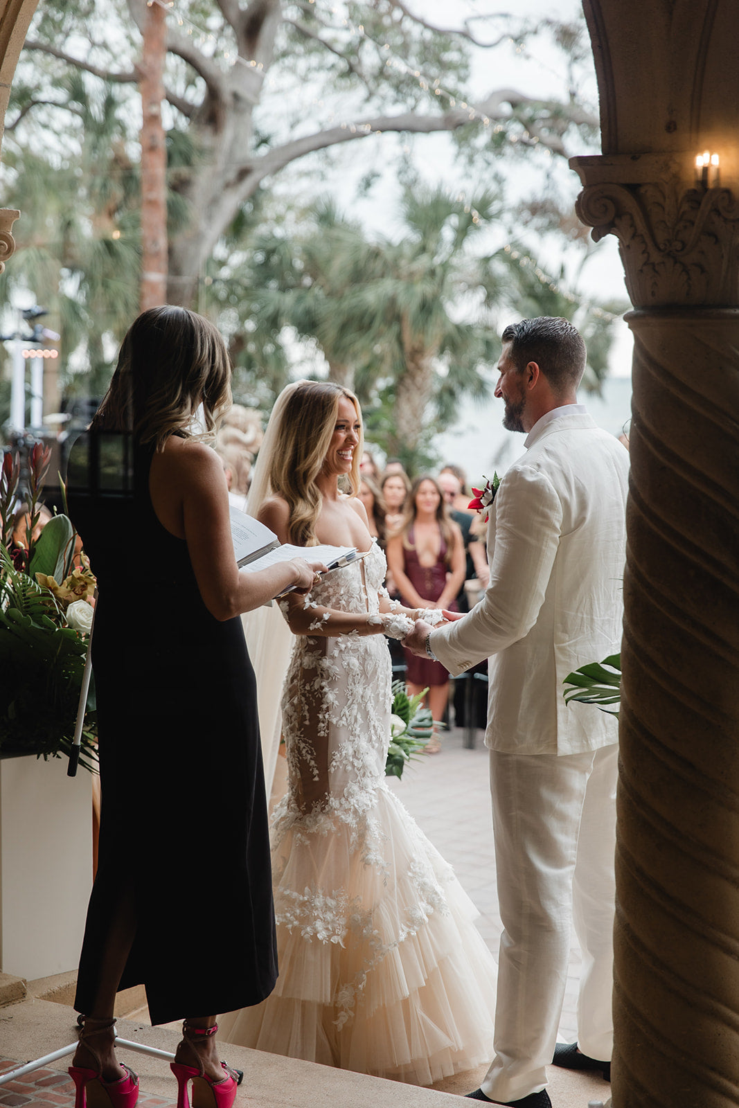 Wedding ceremony with a bride, groom, and officiant outdoors. GL Bride Summer Fox in the lace Veronica dress by Galia Lahav.