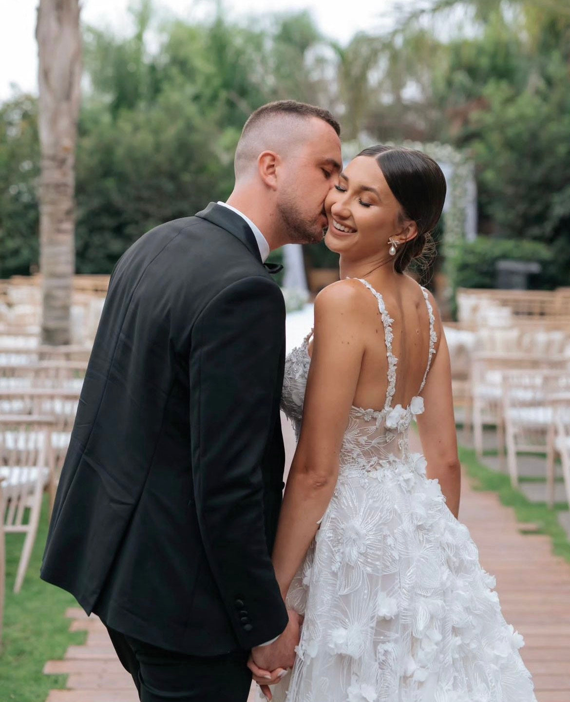 GL Bride Tanya wearing our Fabiana gown  being kissed on the cheek by her husband