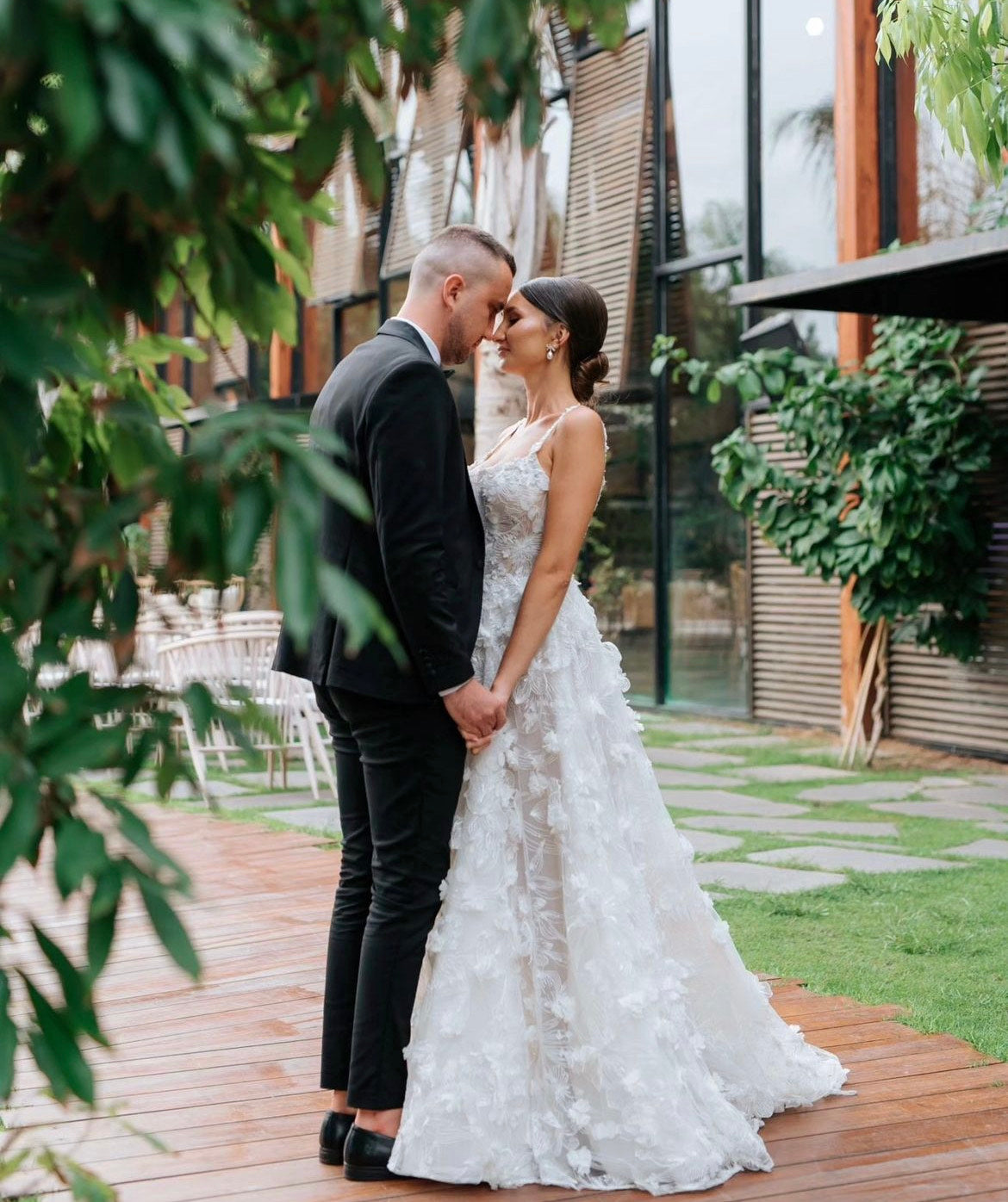 GL Bride Tanya wearing our Fabiana gown standing with her groom surrounded by lush greenery 