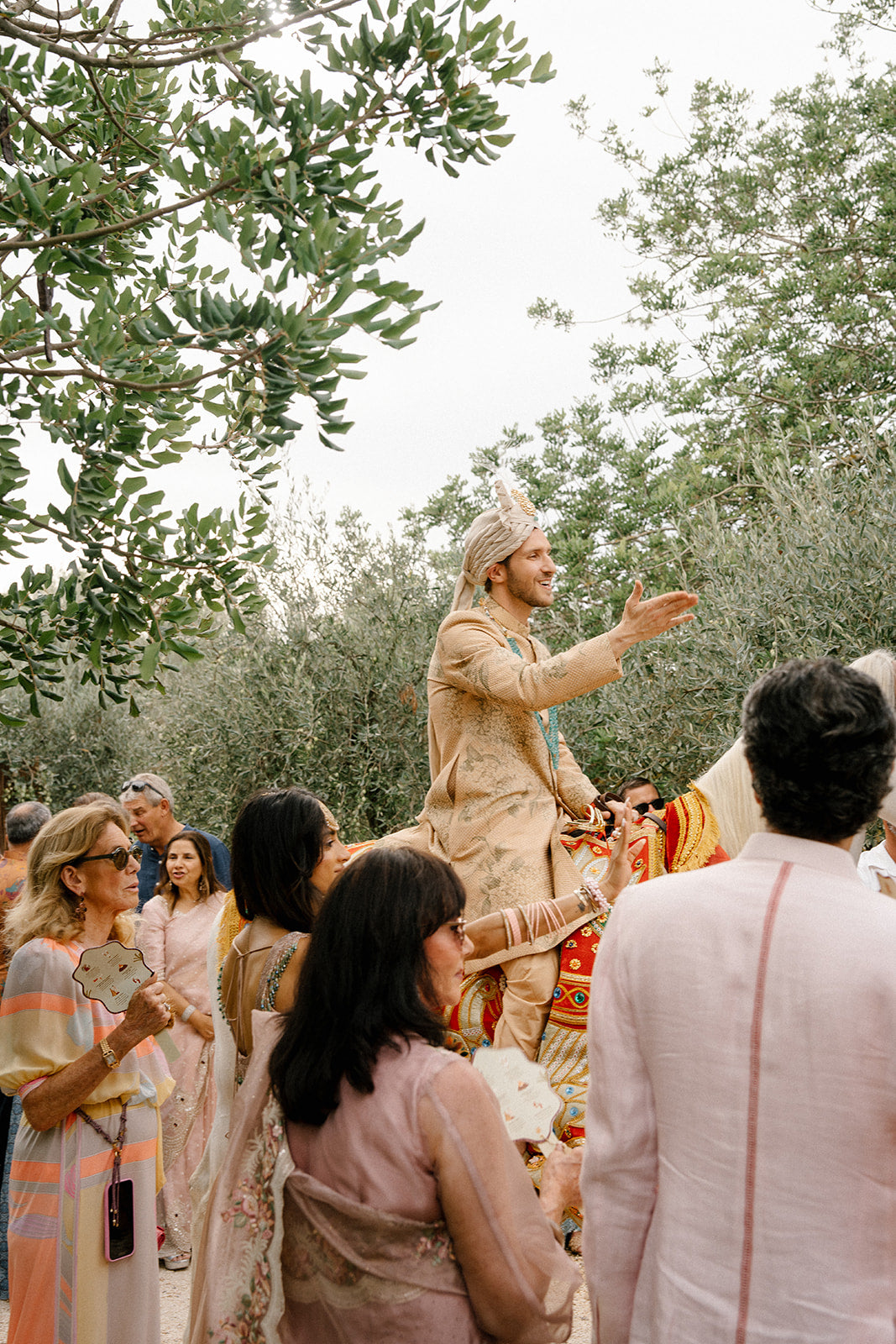 Groom in traditional attire addressing a crowd outdoors with trees in the background
