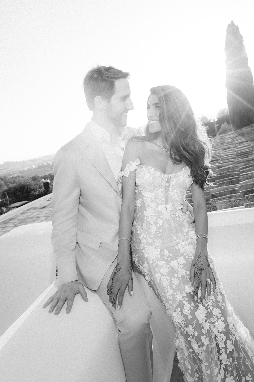 Black and white photo of GL Bride Tara in our Maya gown and her husband in formal attire standing outdoors.