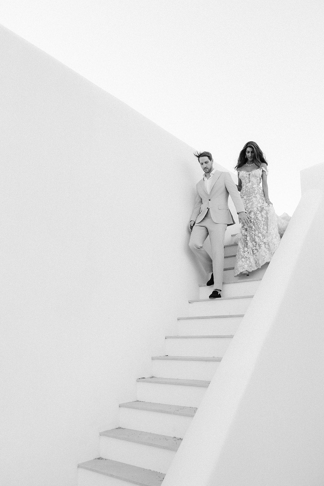 GL Bride Tara in our Maya gown and her husband standing on a white staircase in a minimalistic setting