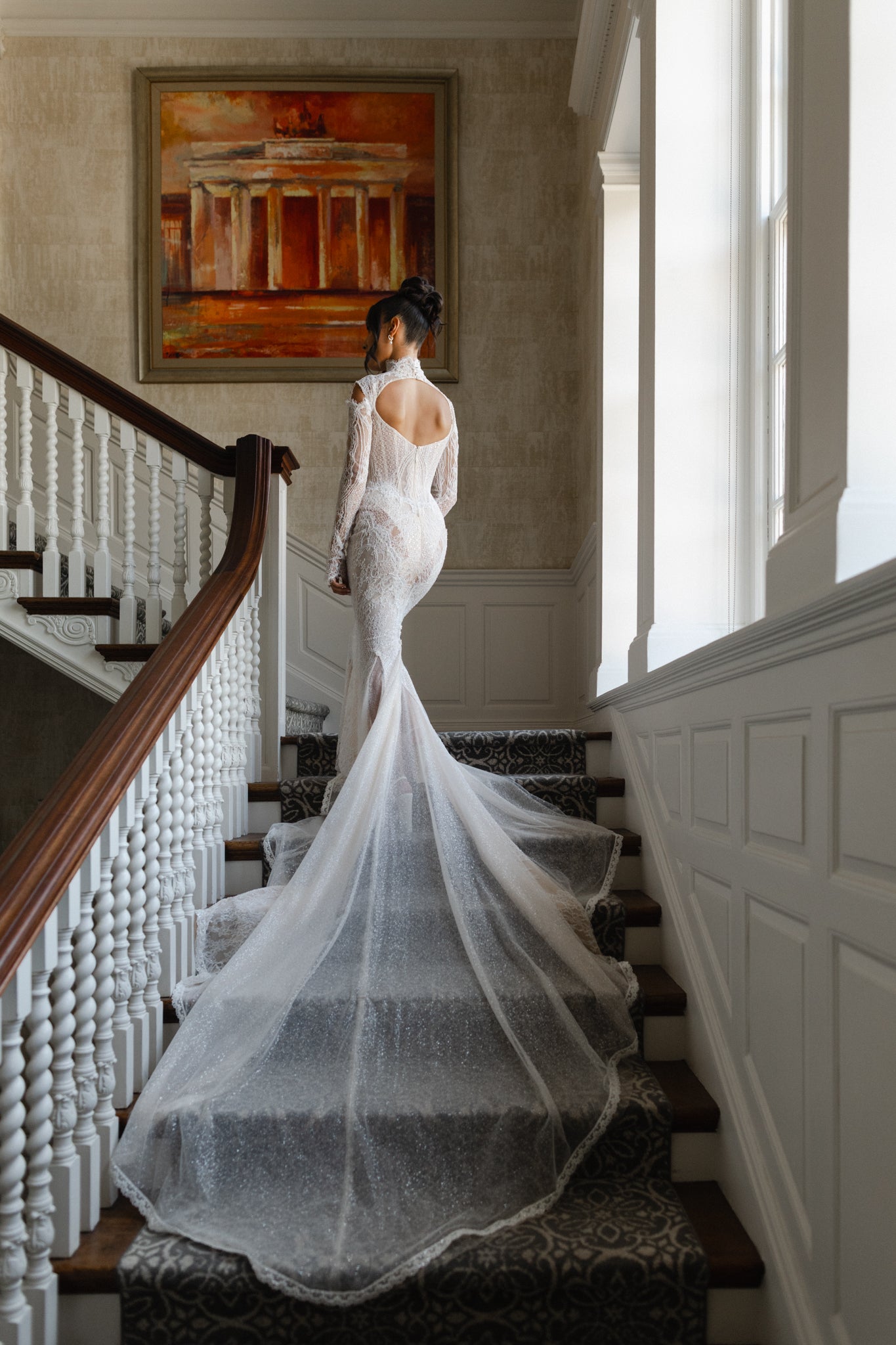 Bride in a white wedding dress standing on a staircase with a painting in the background