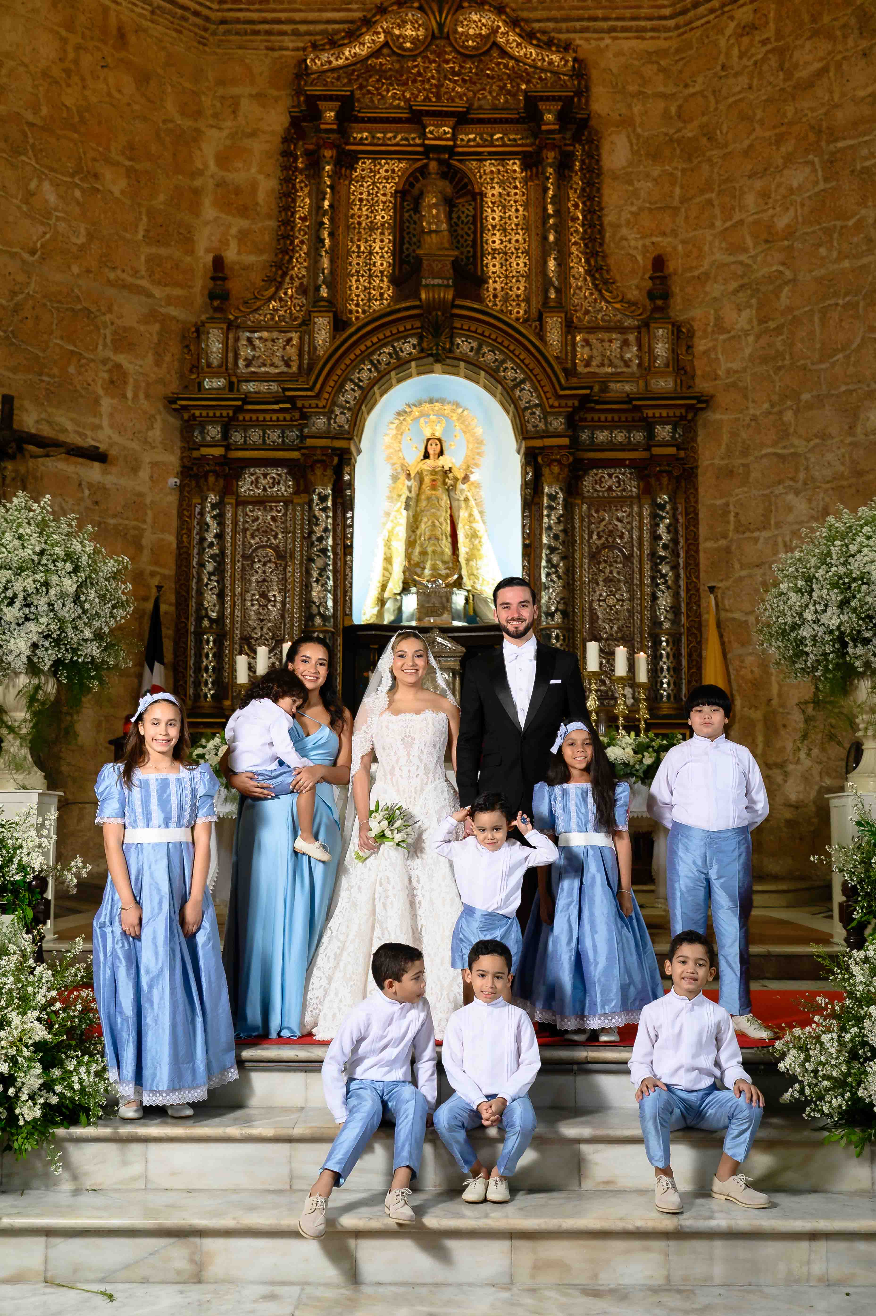 Wedding party posing in front of an ornate altar with floral decorations.