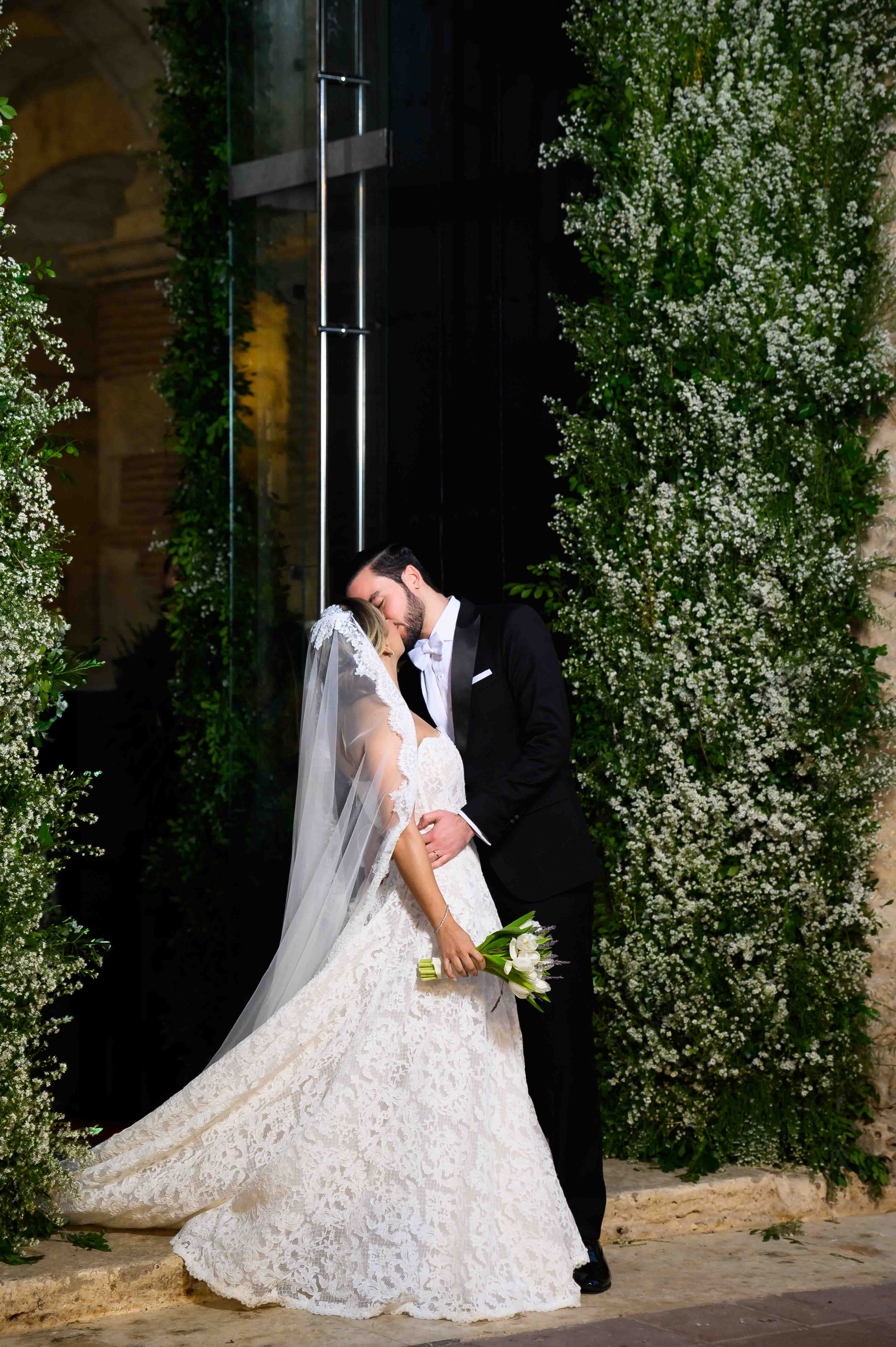 GL Bride Yamilca wearing Galia Lahav's Splendid, embracing  her husband in front of a decorative archway with greenery.