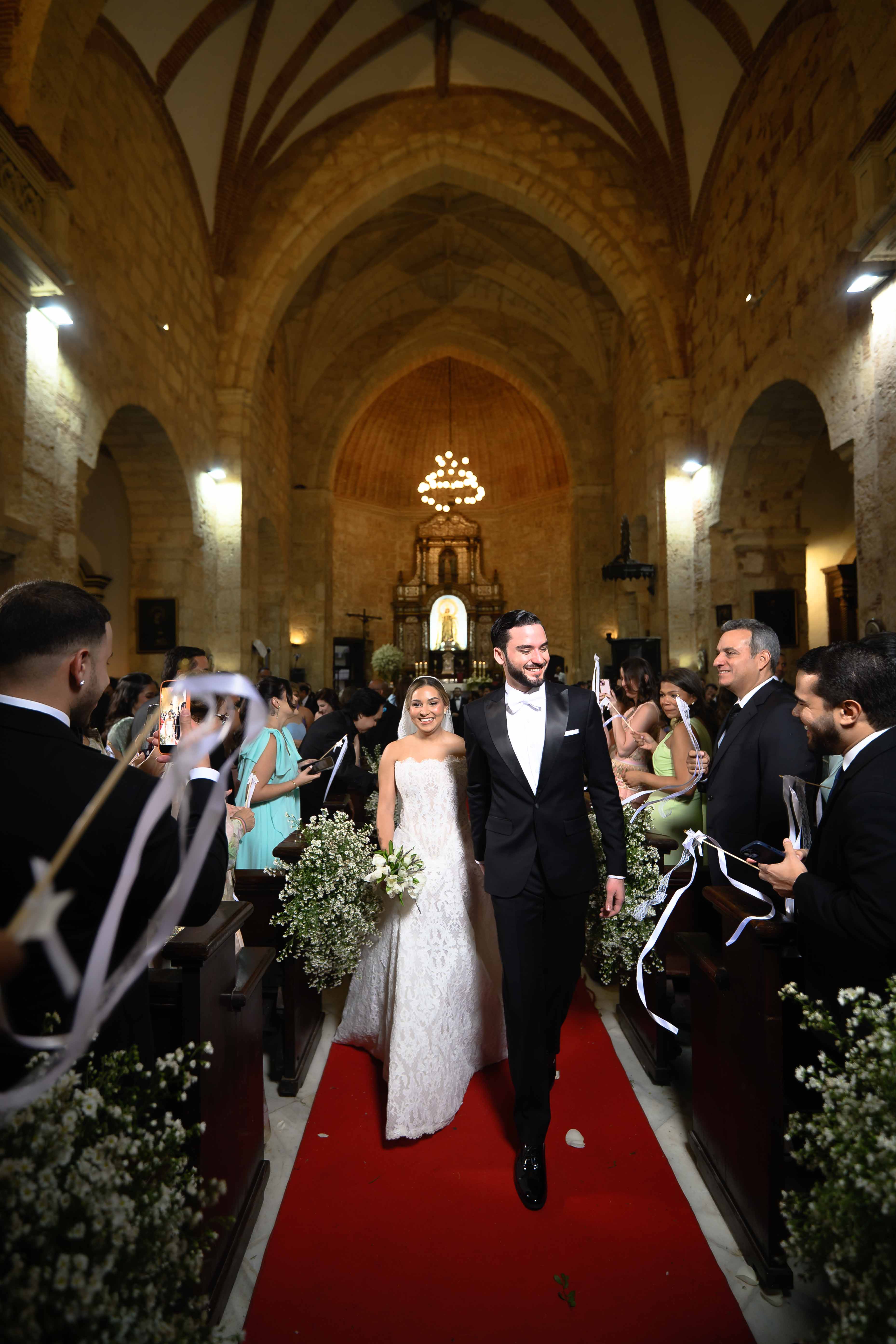 GL Bride Yamilca wearing our Splendid  and her husband walking down a red carpet in an elegant church setting.