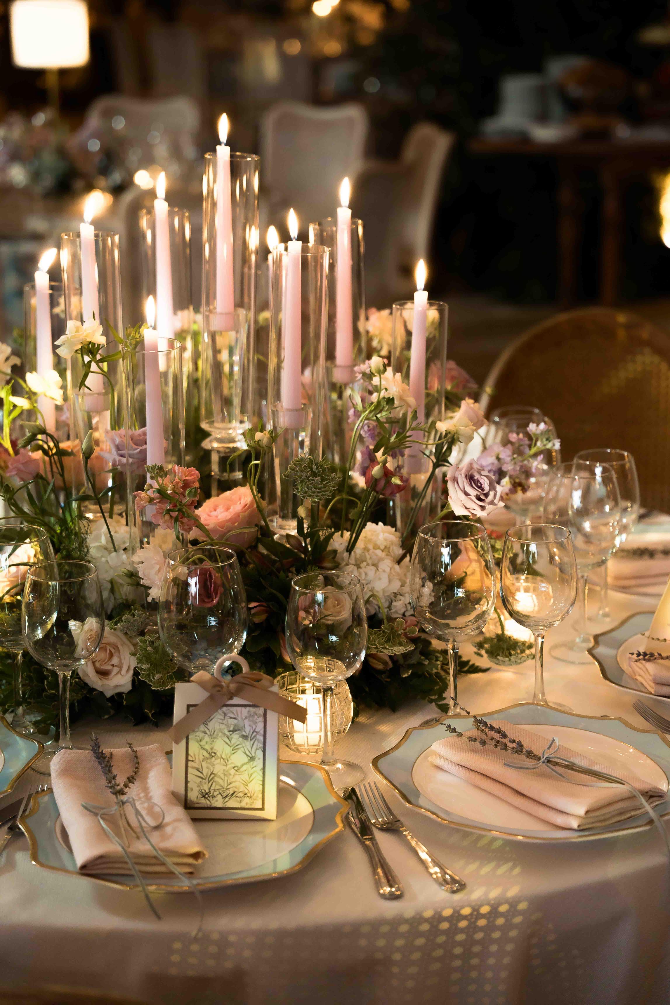 Elegant table setting with candles, flowers, and cutlery on a white tablecloth.