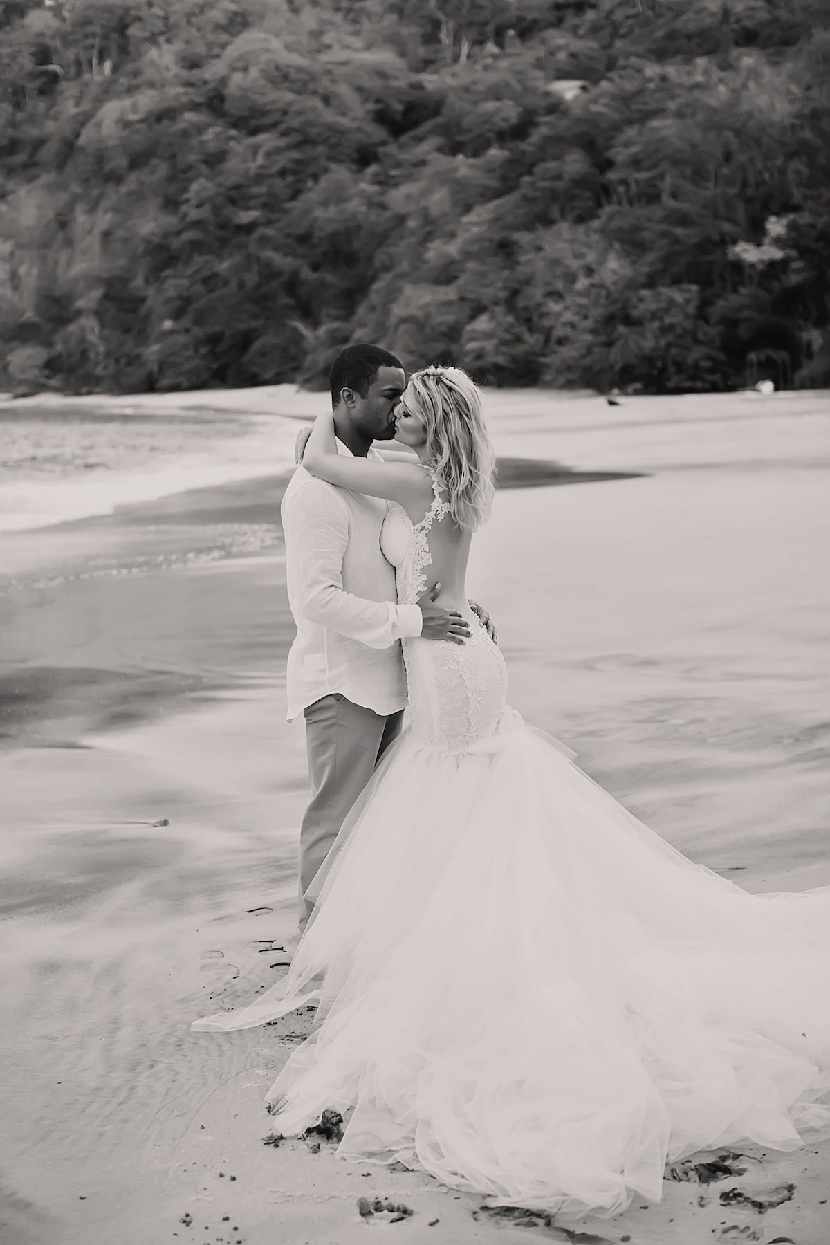 GL Bride Allie wearing our Loretta gown kissing her husband on the beach 