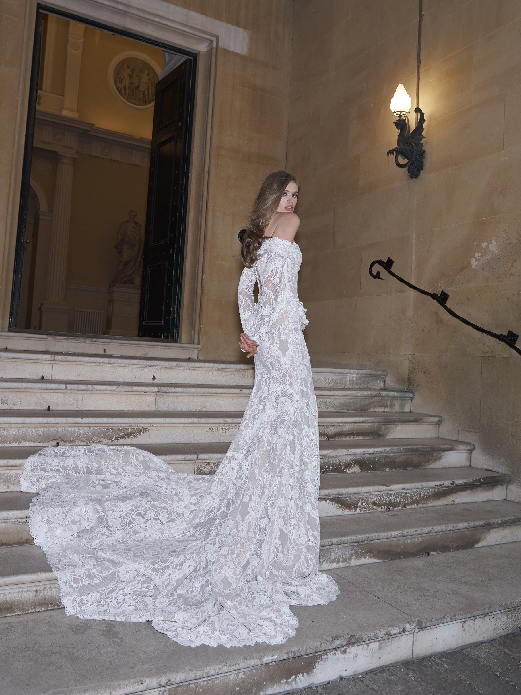 Woman in a white lace wedding dress standing on stone steps.