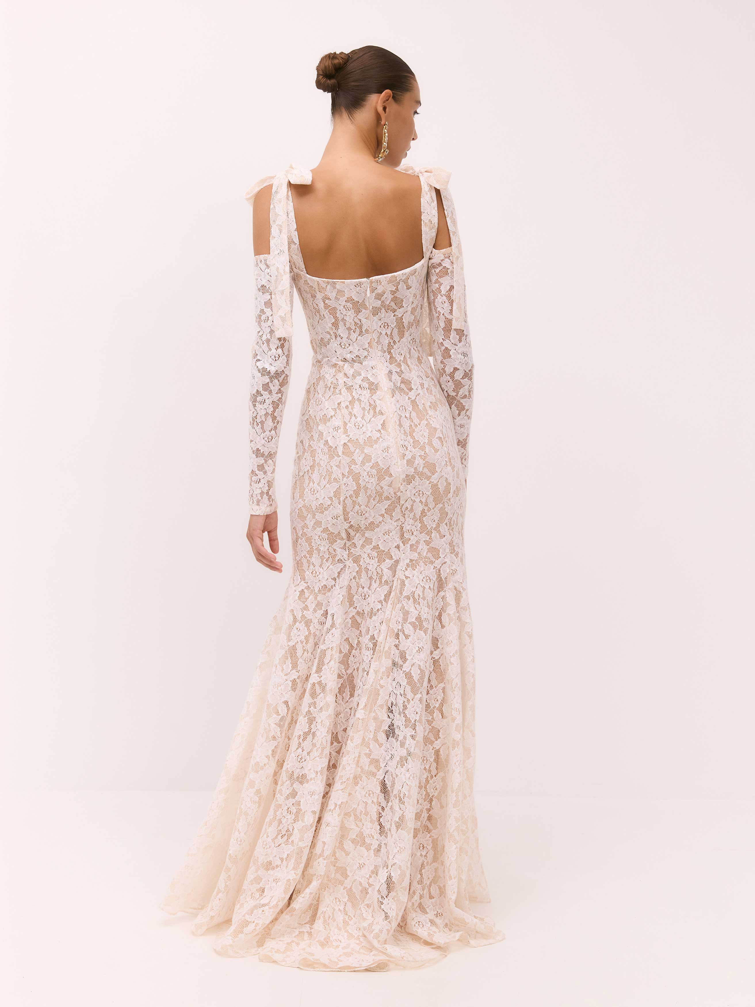 Woman wearing a long, floral lace dress with thin straps on a white background