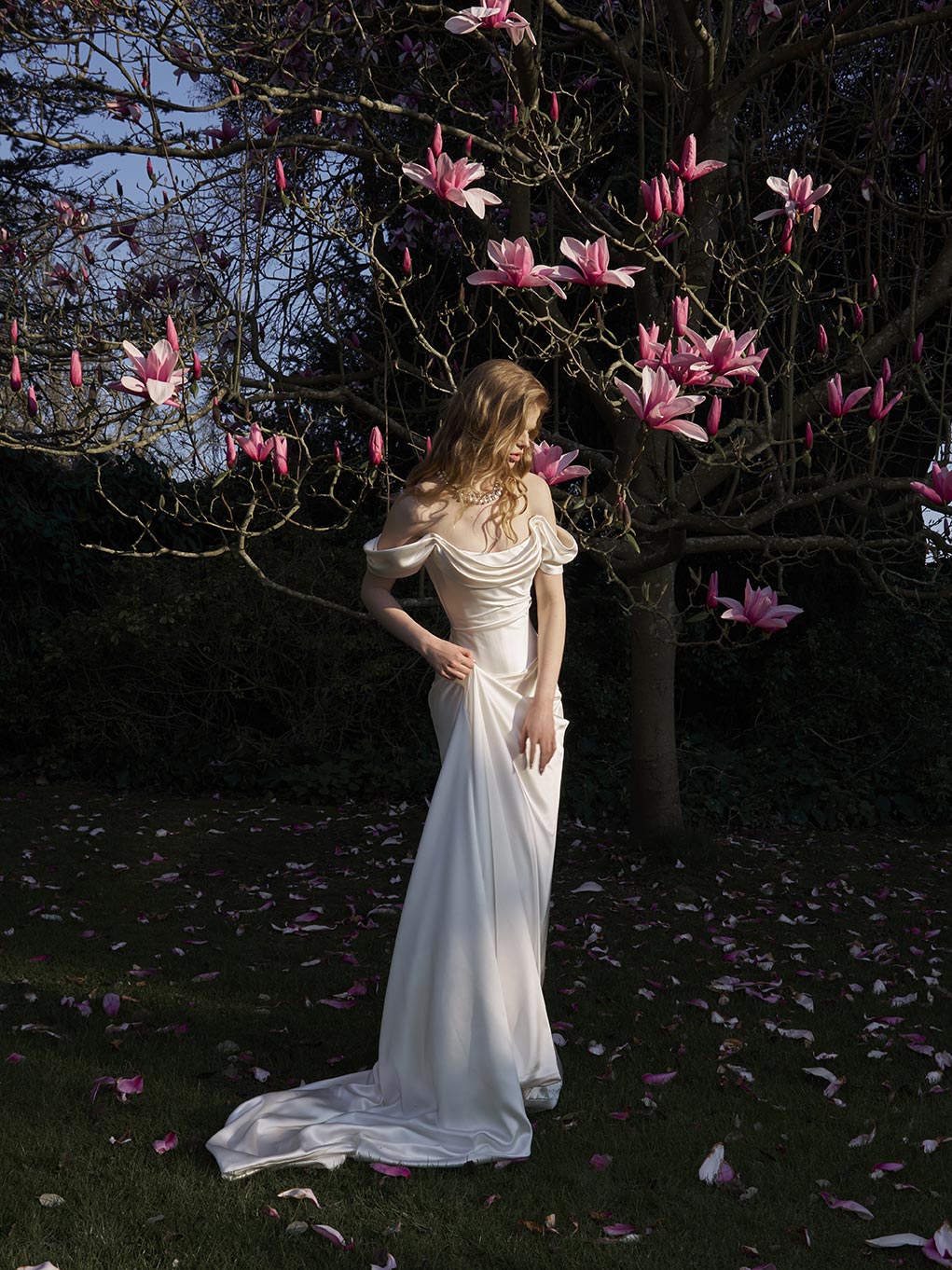 Woman in a white dress standing under a tree with pink flowers