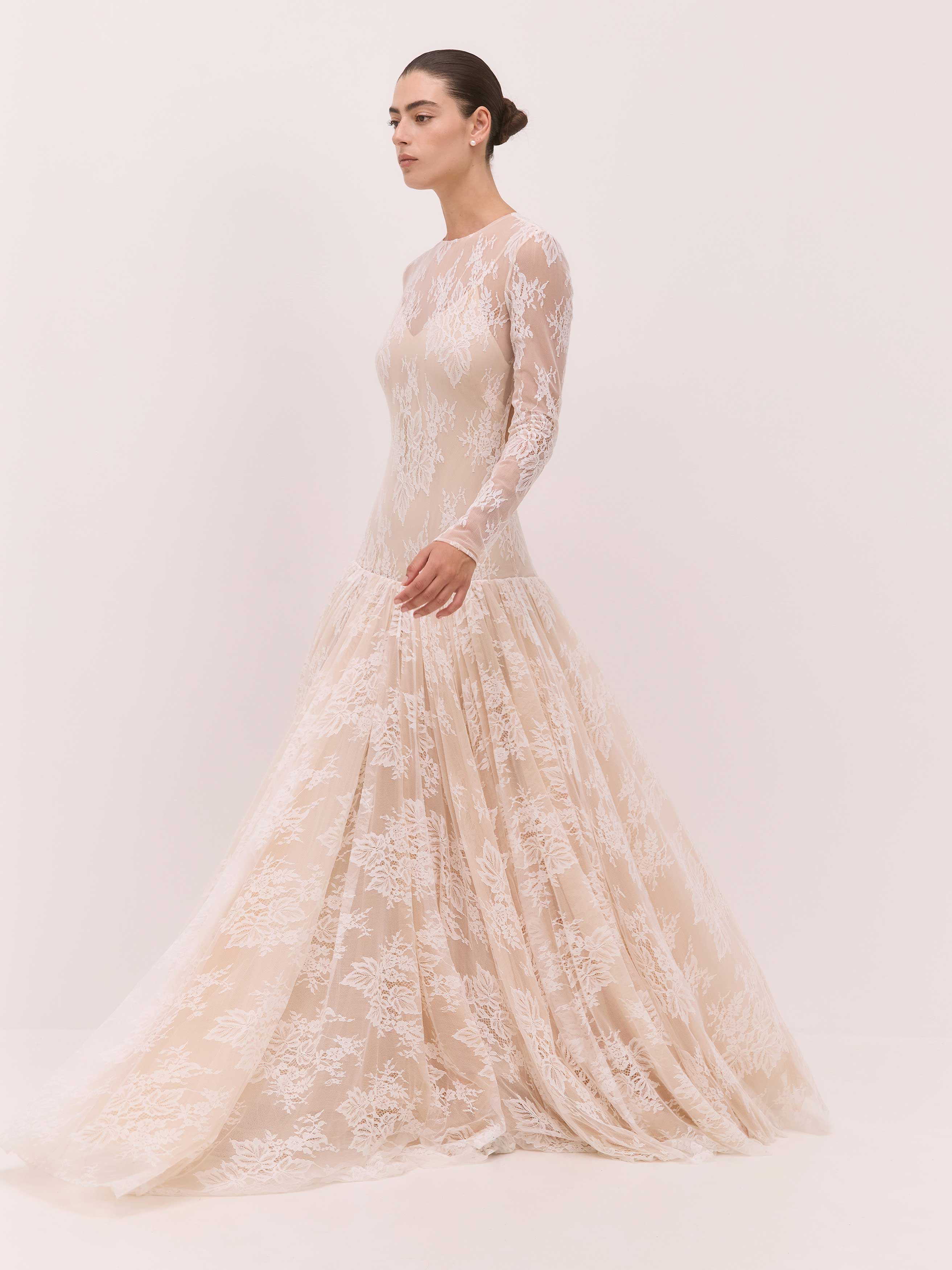 Woman wearing a long-sleeve lace wedding dress against a plain background