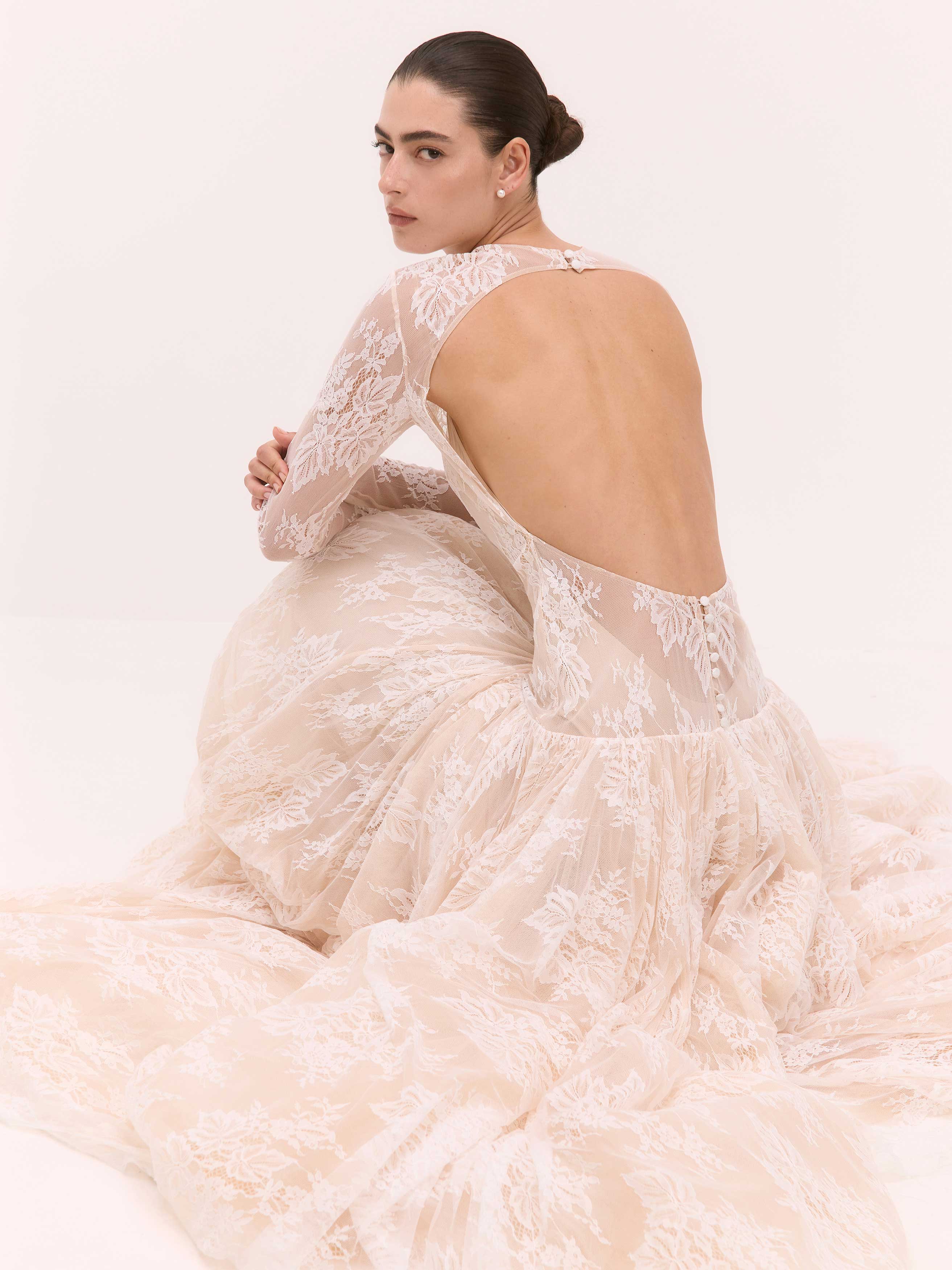 Woman wearing a beige lace wedding dress with a low back on a white background