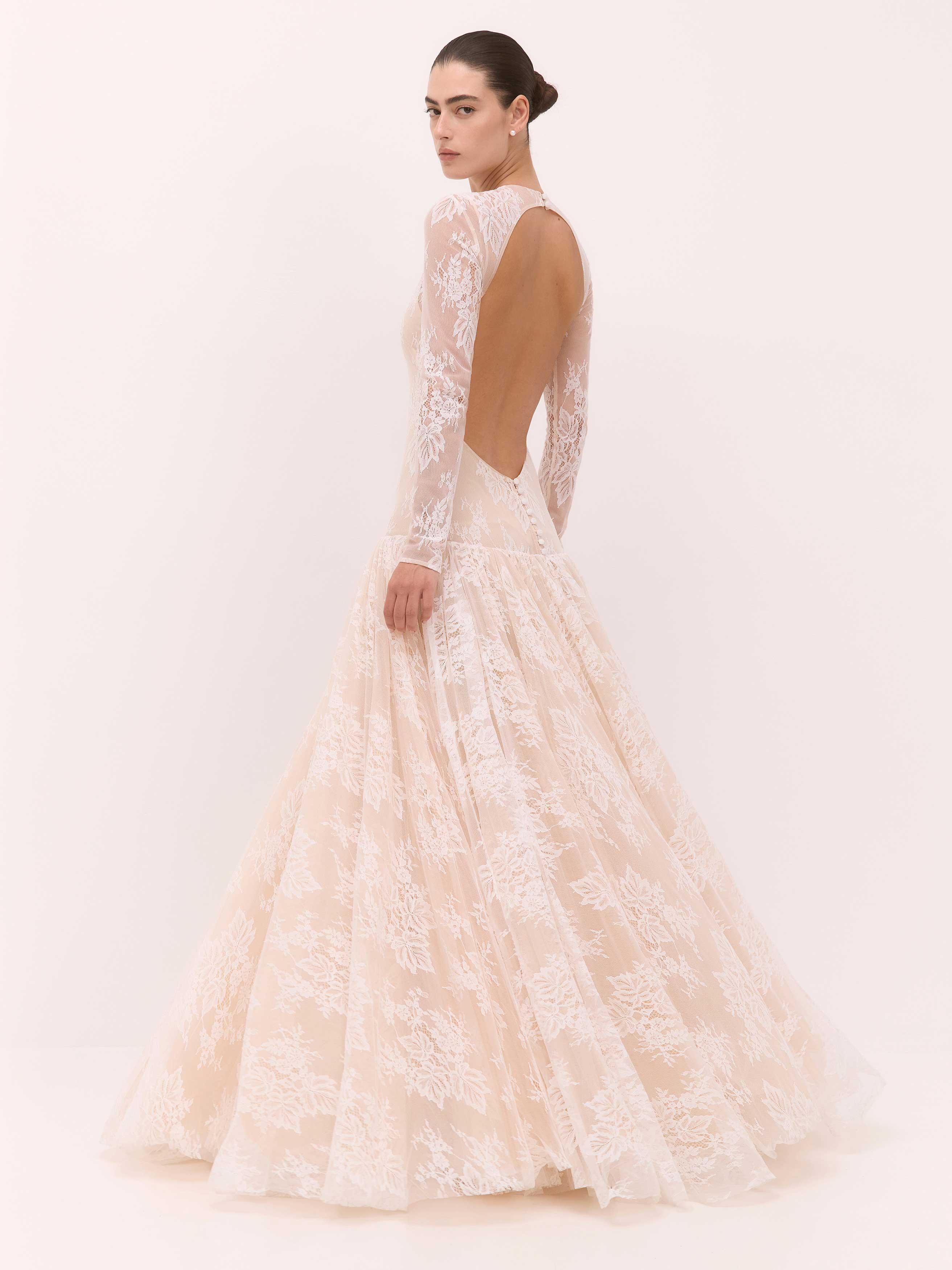 Woman wearing a lace wedding dress with a sheer back on a white background