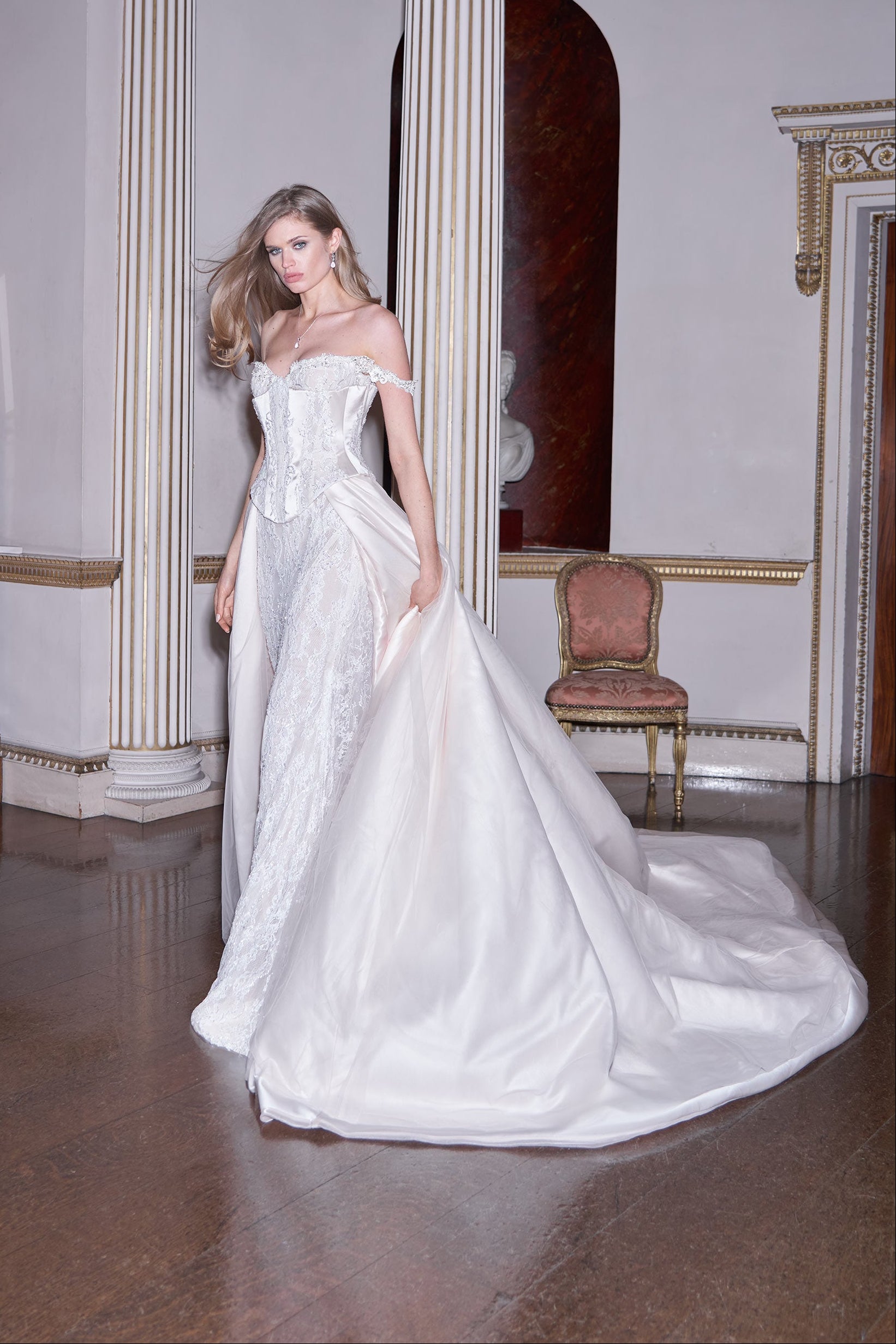 Woman in a white wedding dress standing in an elegant room with columns and a chandelier.
