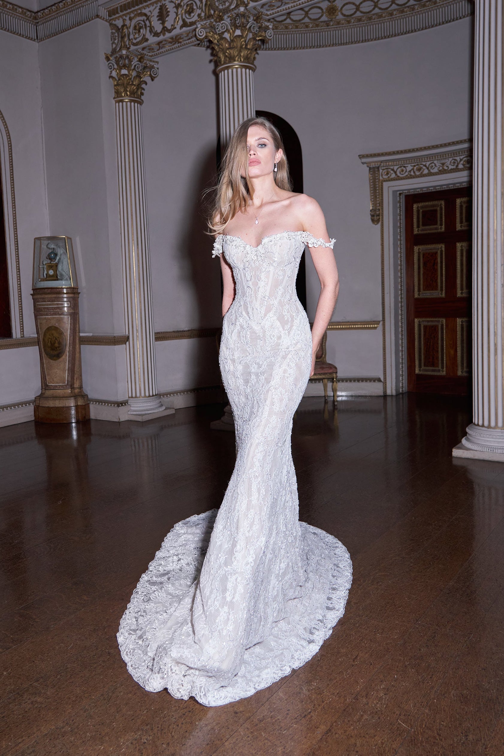 Woman in a white lace wedding dress standing in an elegant room with classical architecture.