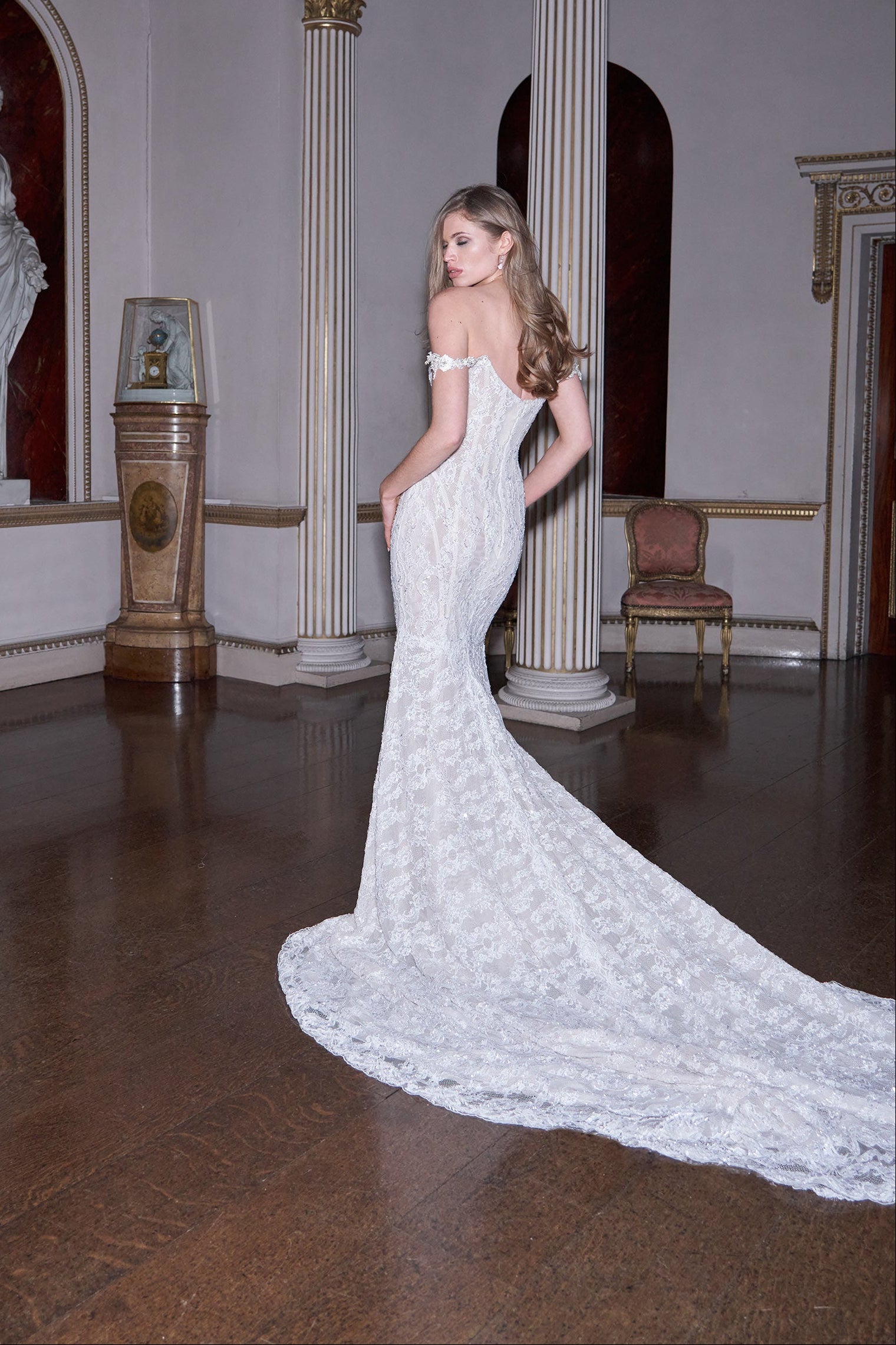 Woman in a white lace wedding dress standing in an elegant room with classical architecture.