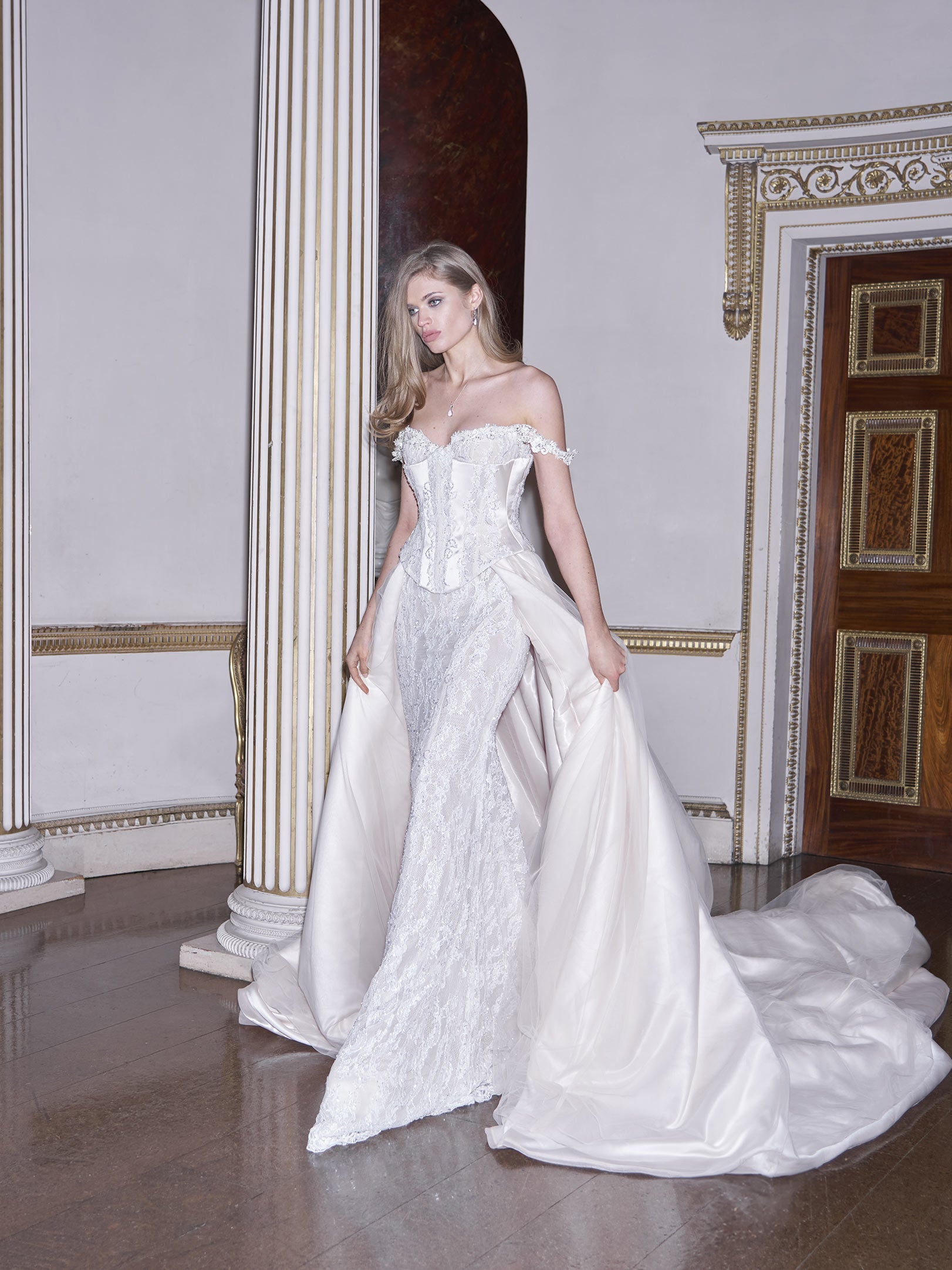 Woman in a white wedding dress standing in an elegant room with decorative columns and moldings.