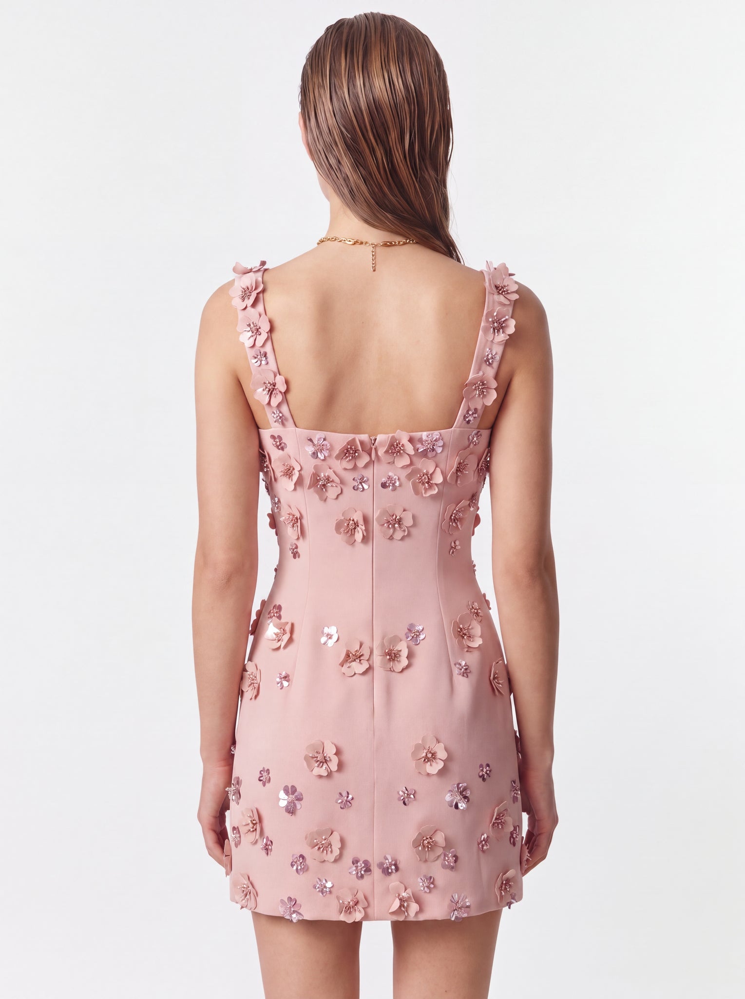 A model shown from the back wearing a light pink sleeveless mini dress with 3D floral appliqués and sequined details on a plain white studio background.