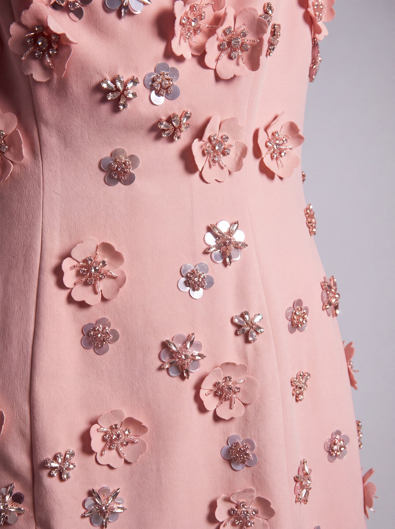 Close-up of a light pink dress or garment covered with 3D floral appliqués and metallic flower embellishments in rose gold and silver tones.