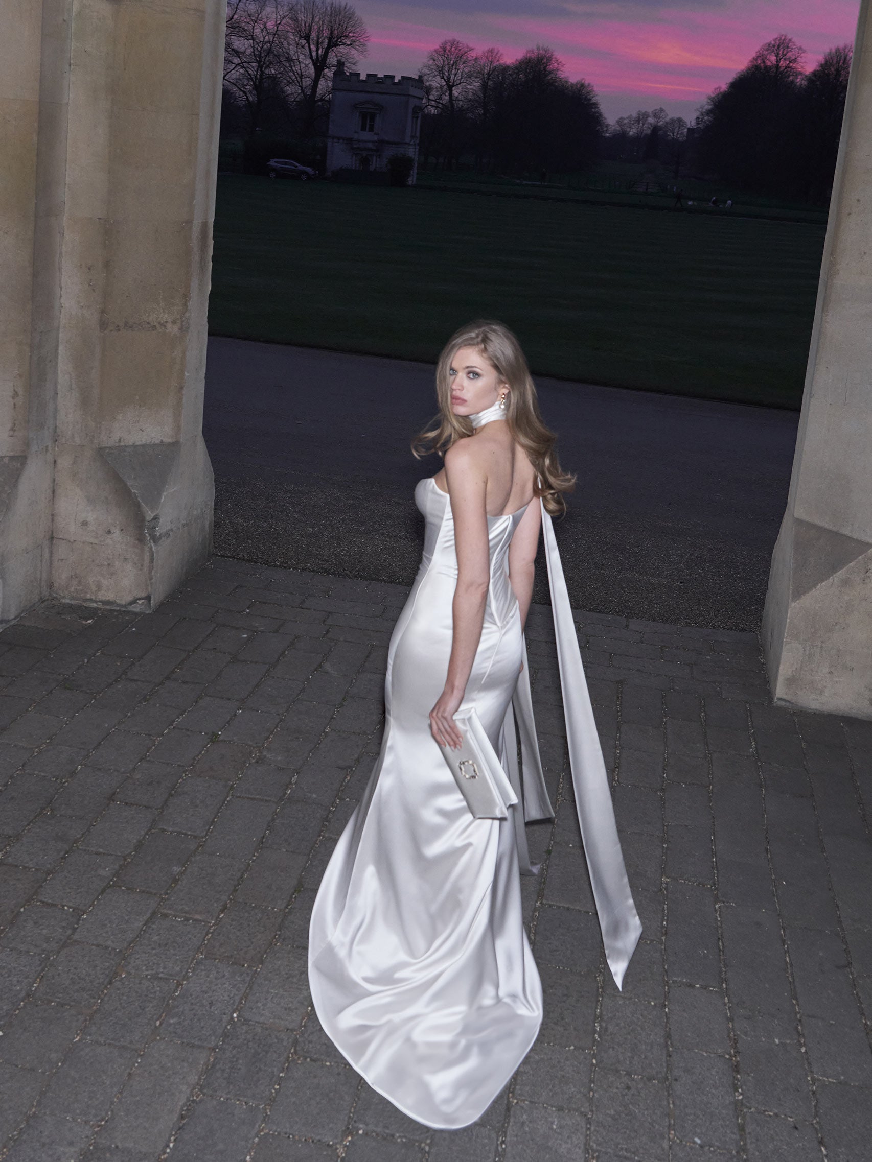 Woman in a white wedding dress standing in an outdoor setting with a sunset sky.
