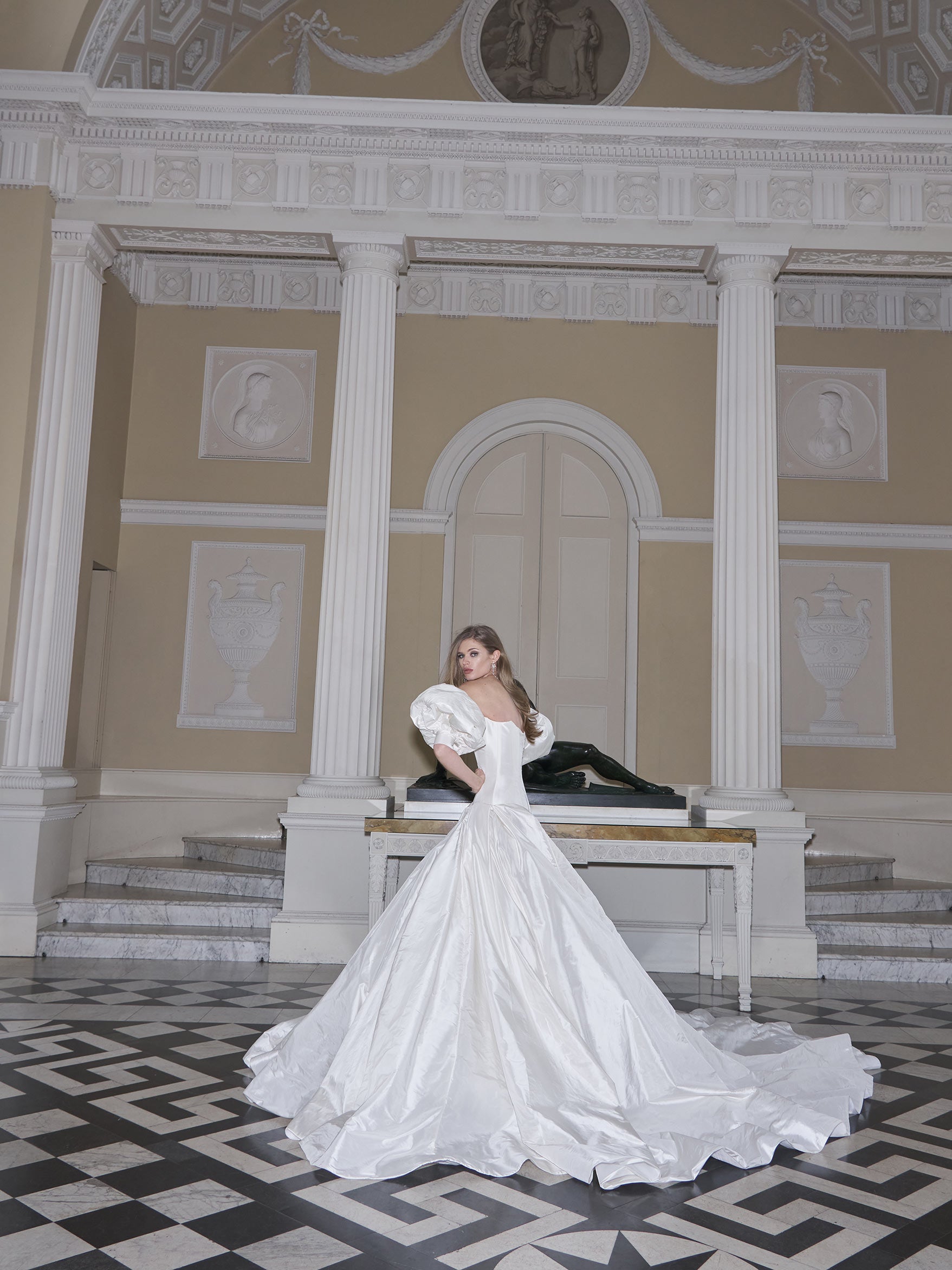 Woman in a white wedding dress standing in an elegant interior setting with decorative columns and a black grand piano.