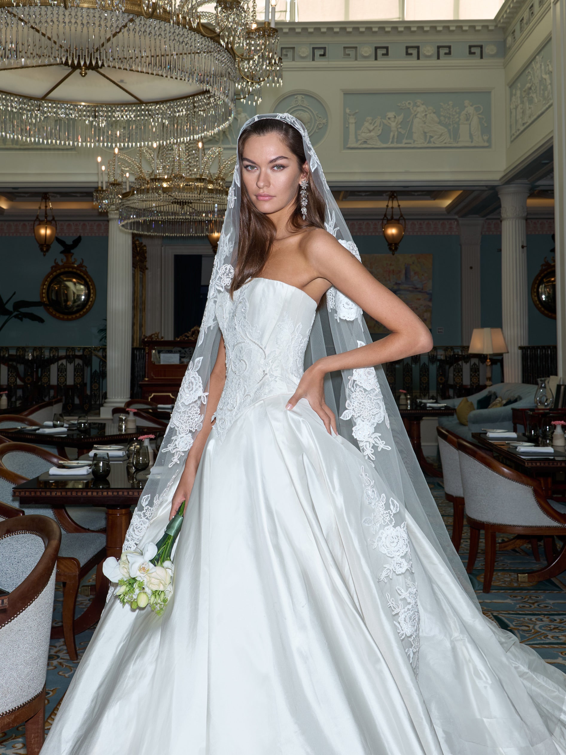 Bride in a white wedding dress with a long veil standing in an elegant indoor setting.