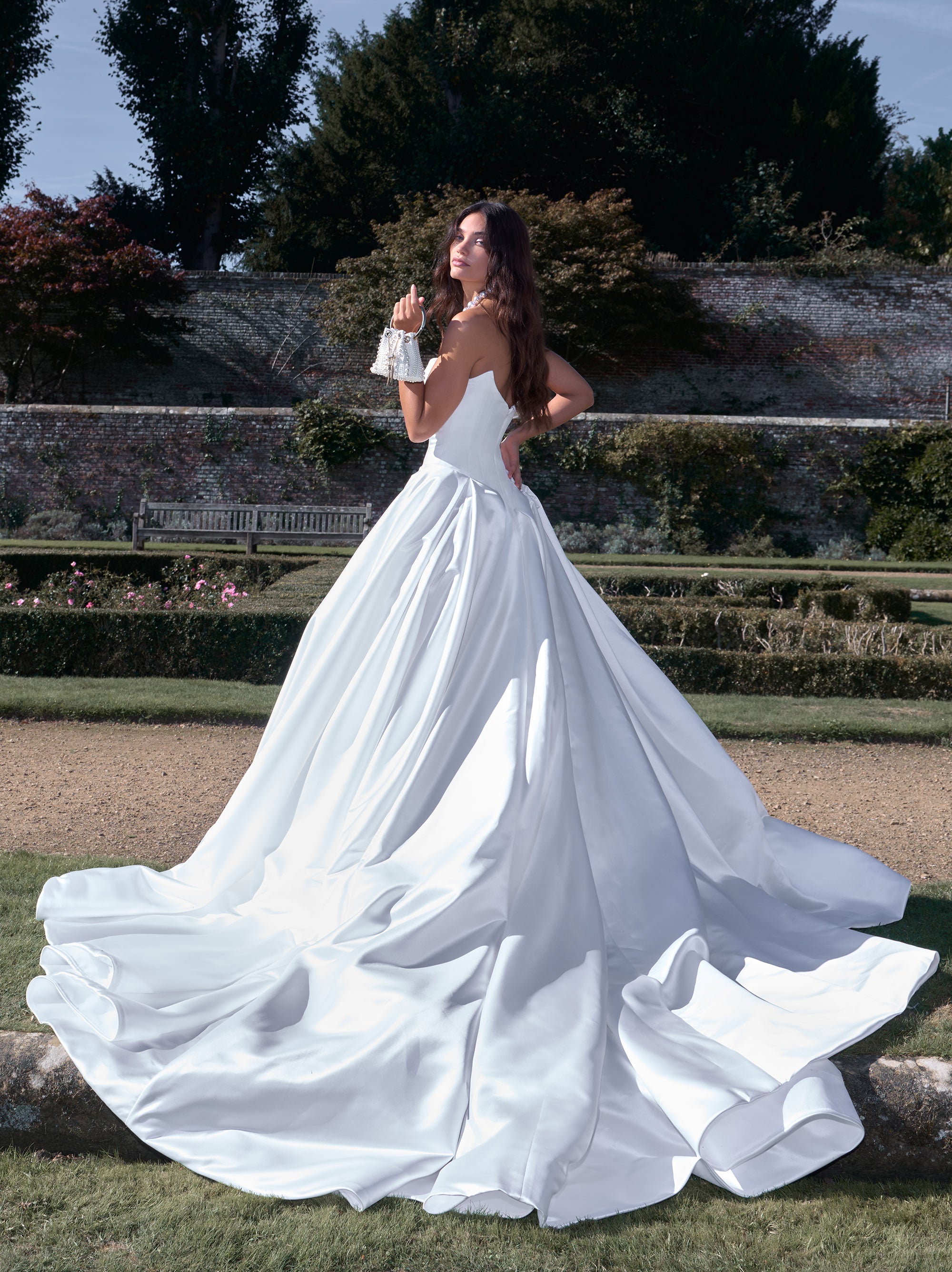 Woman in a white wedding dress standing outdoors with greenery in the background