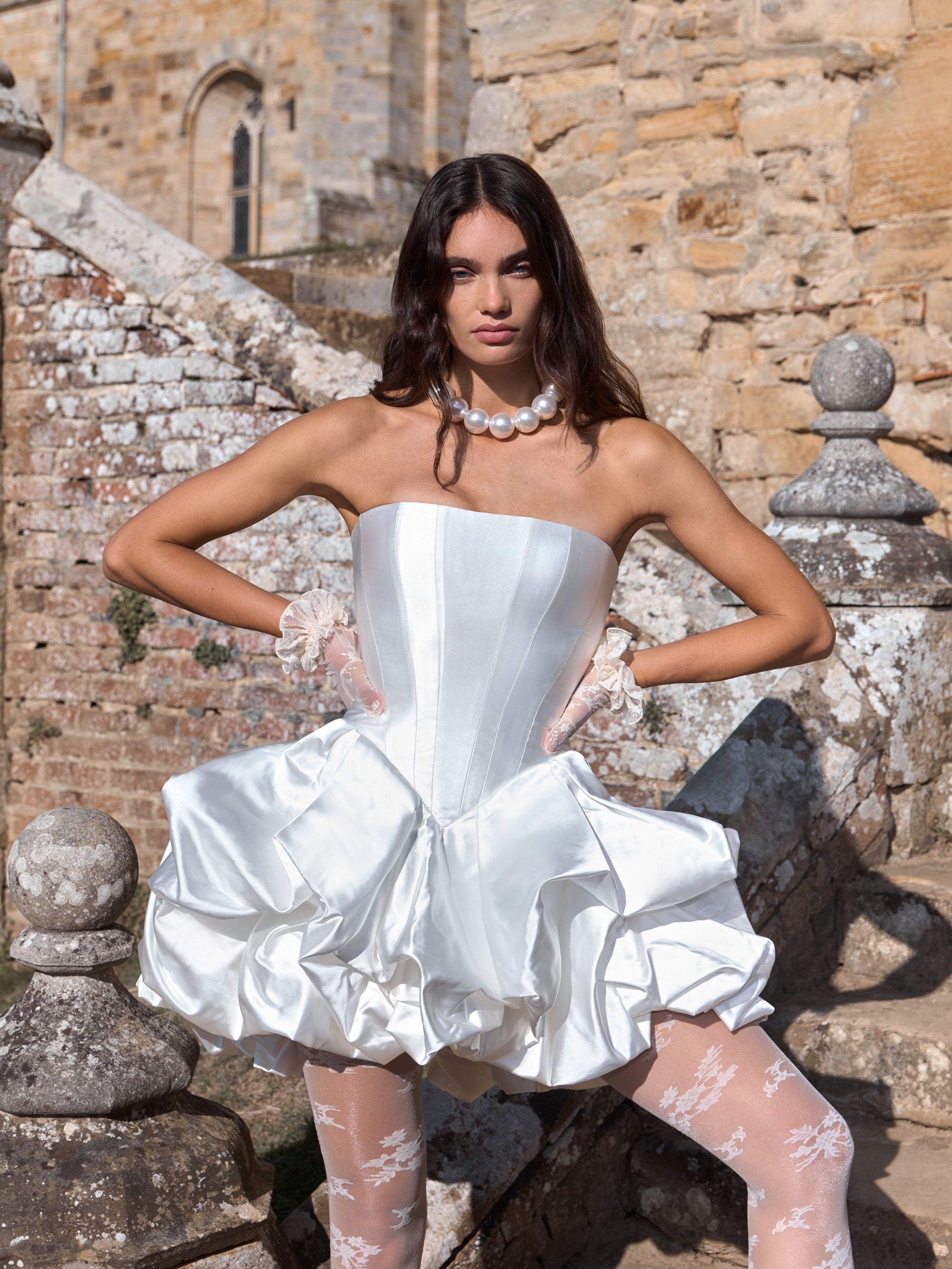 Woman in a white strapless dress standing in front of a stone wall.