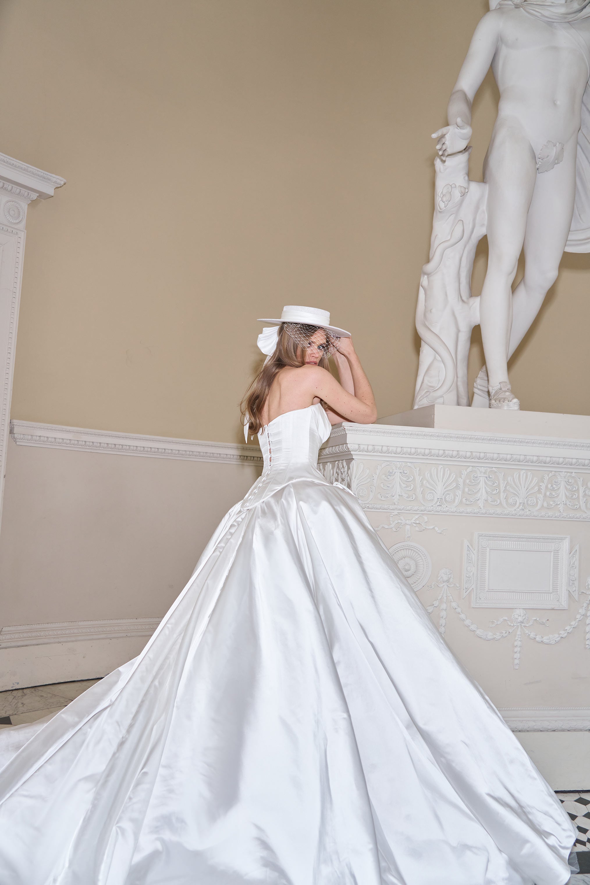 Woman in a white wedding dress standing in a classical setting with a statue.