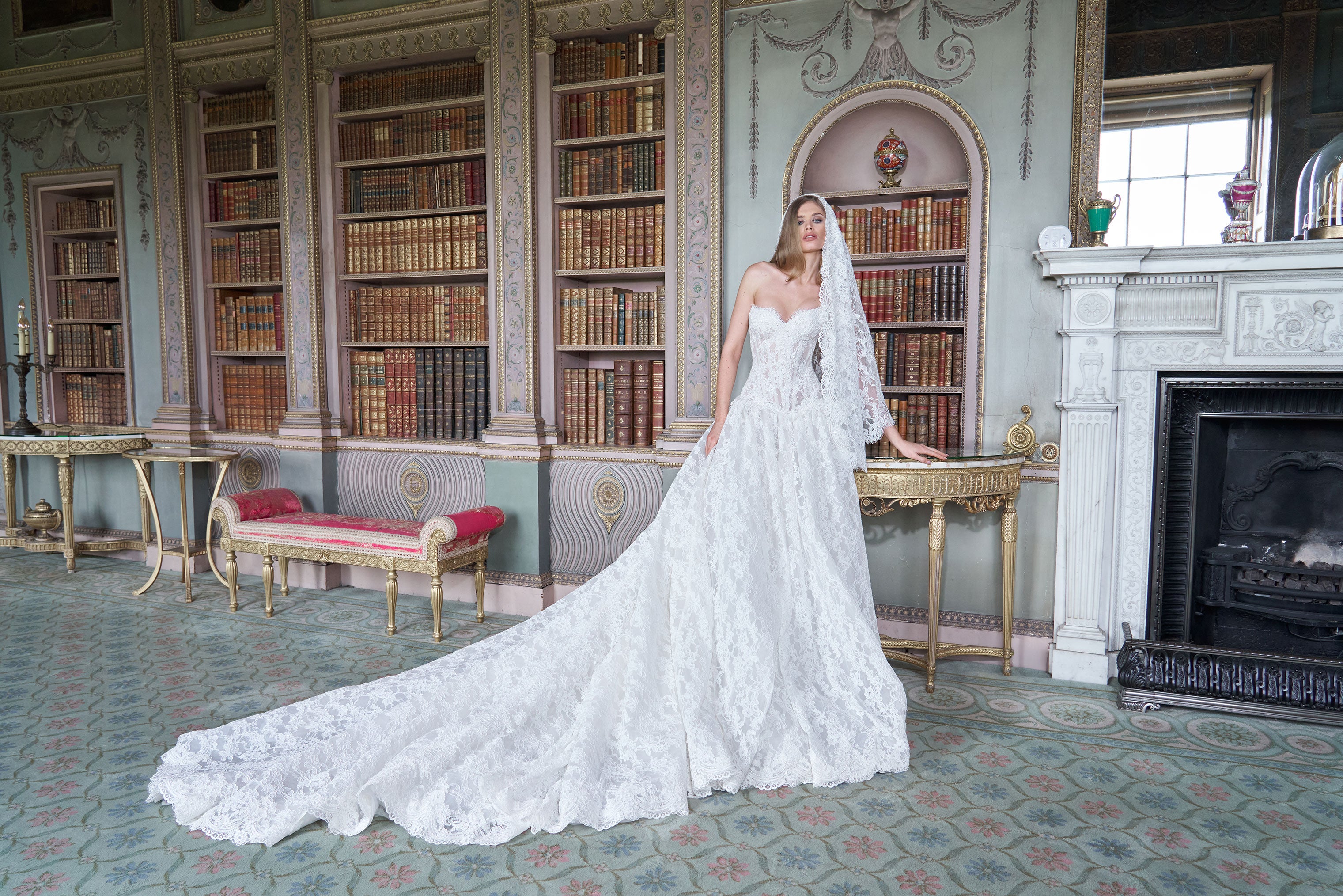 Woman in a white wedding dress standing in an elegant room with bookshelves and a fireplace.