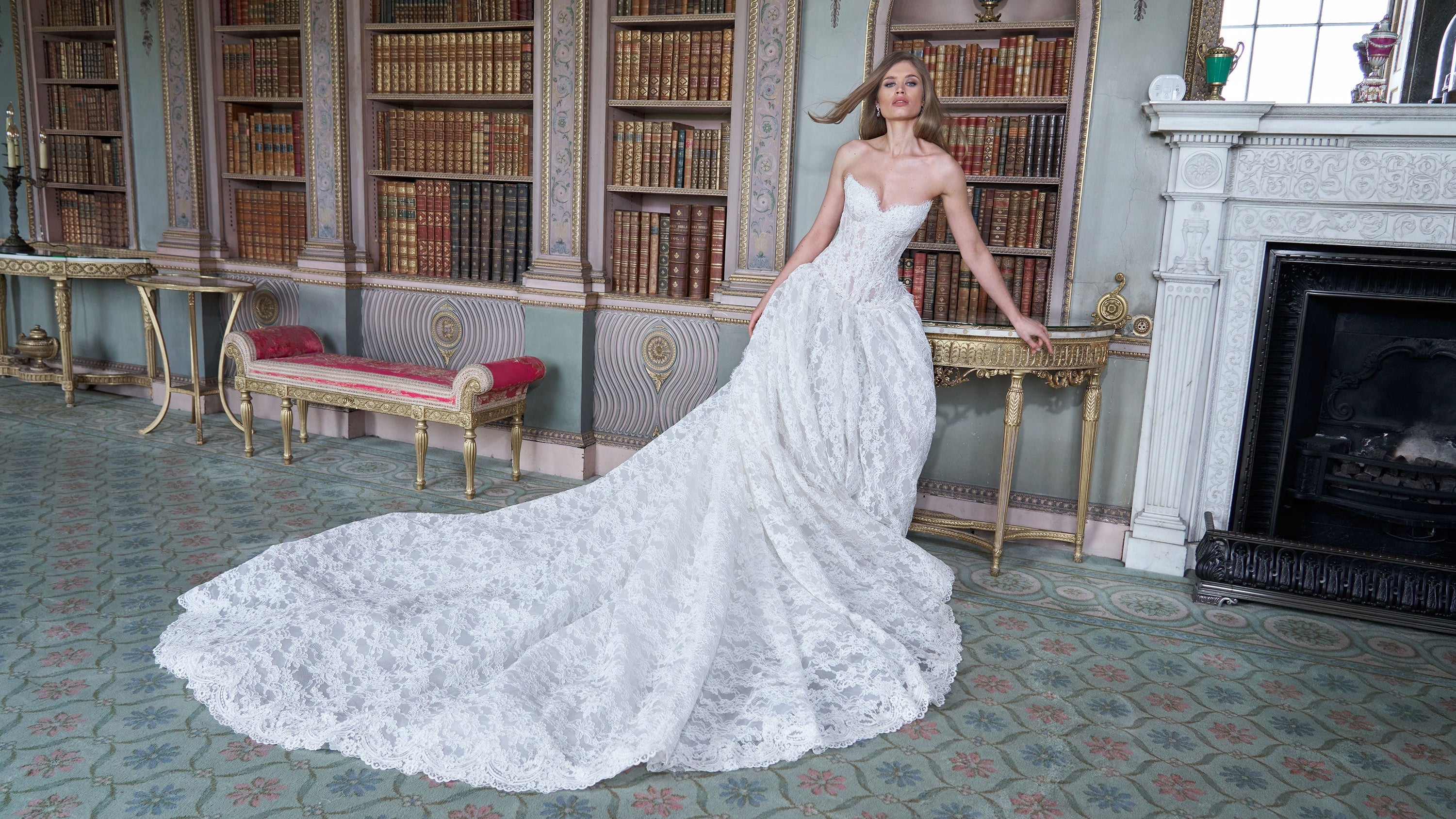 Woman in a white wedding dress standing in a grand room with bookshelves and a fireplace.