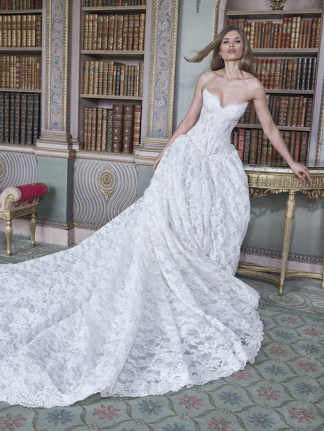 Woman in a white lace wedding dress standing in a room with bookshelves.