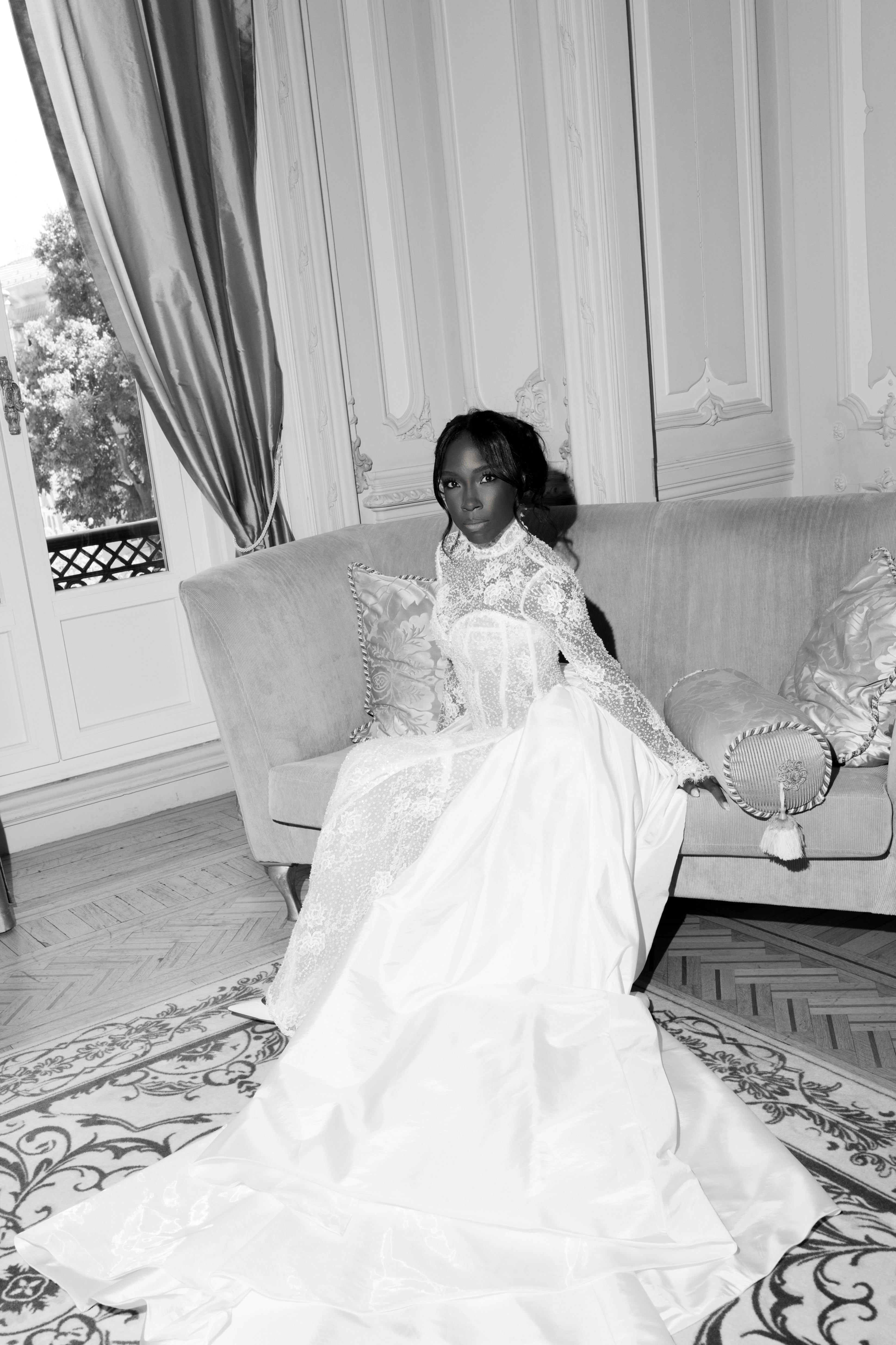 Woman in a formal gown sitting on a couch in an elegant room.