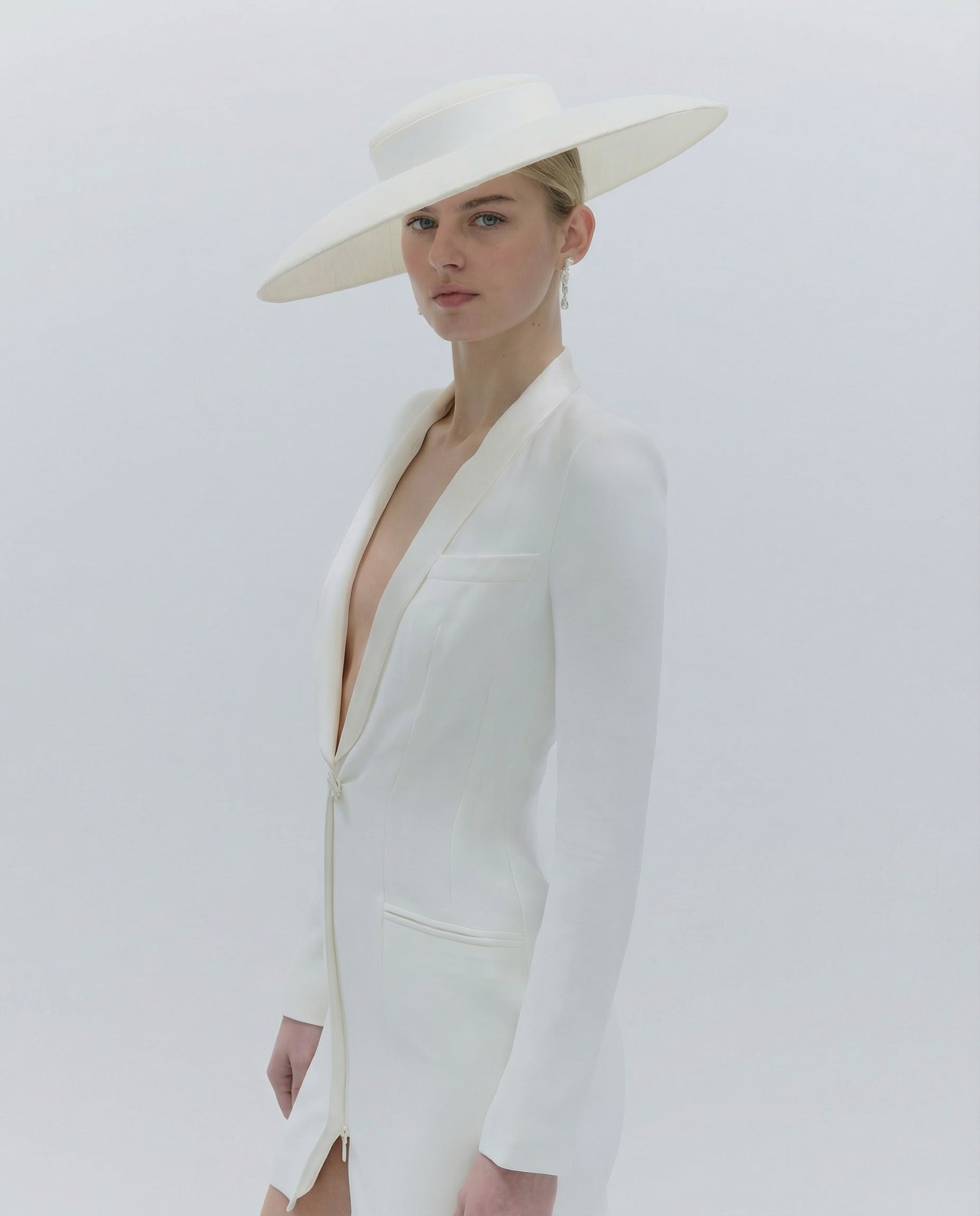 Woman wearing a white outfit with a wide-brimmed hat on a plain background