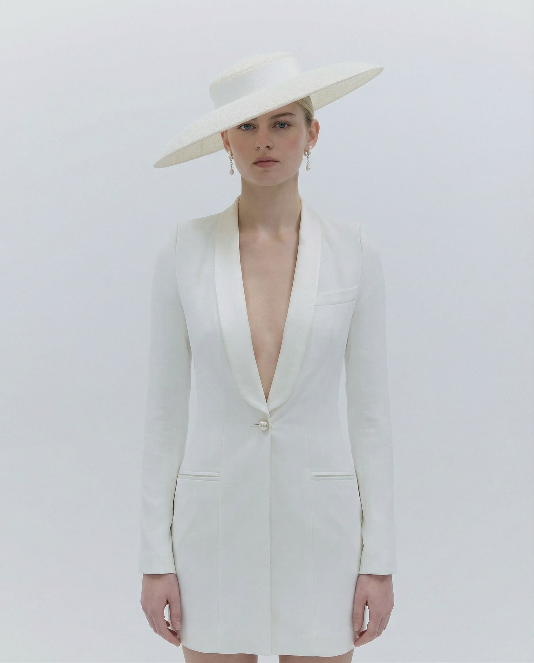 Woman wearing a white blazer dress and hat on a light gray background