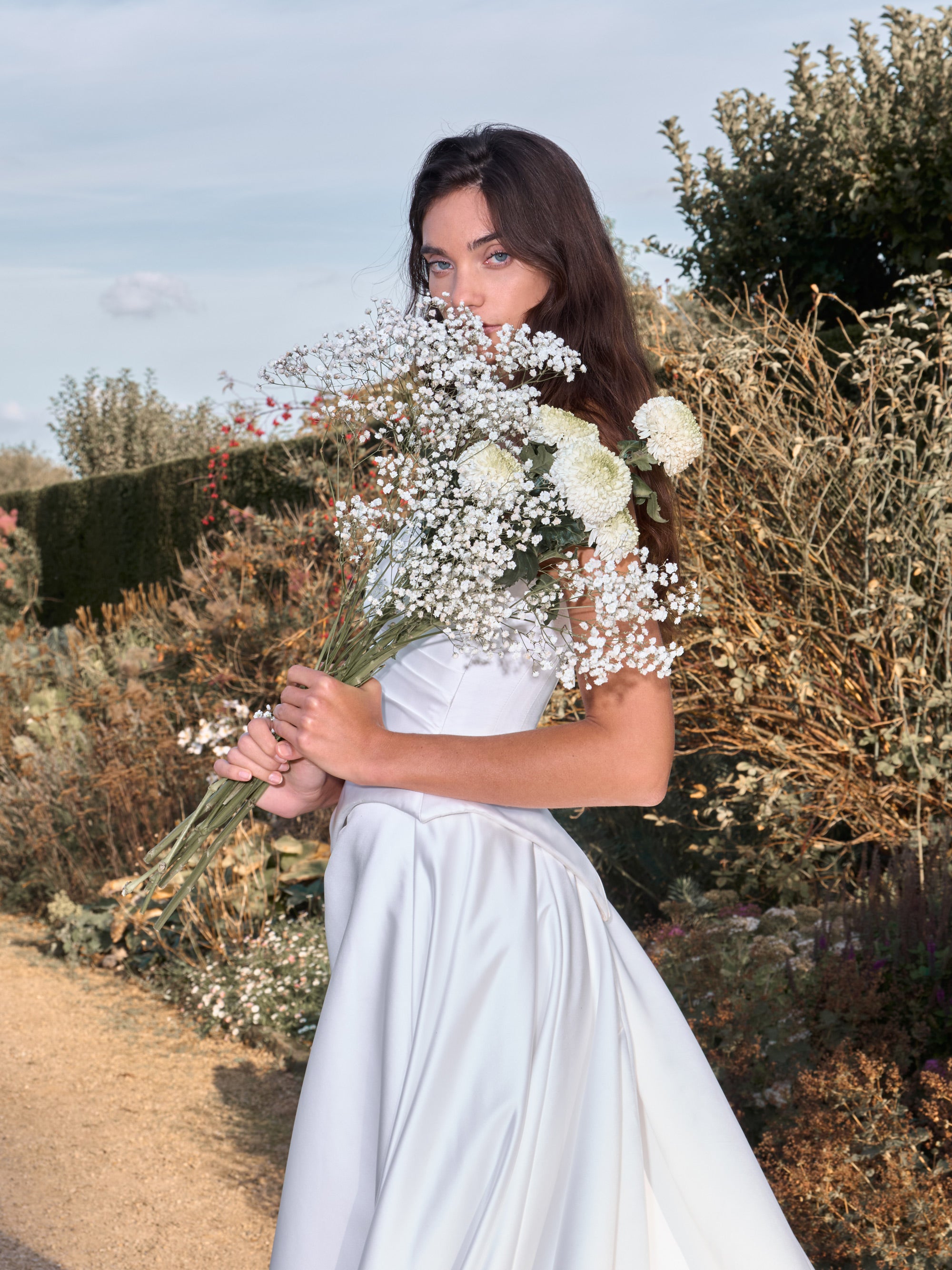 Woman in a white dress holding a bouquet of flowers in a natural setting