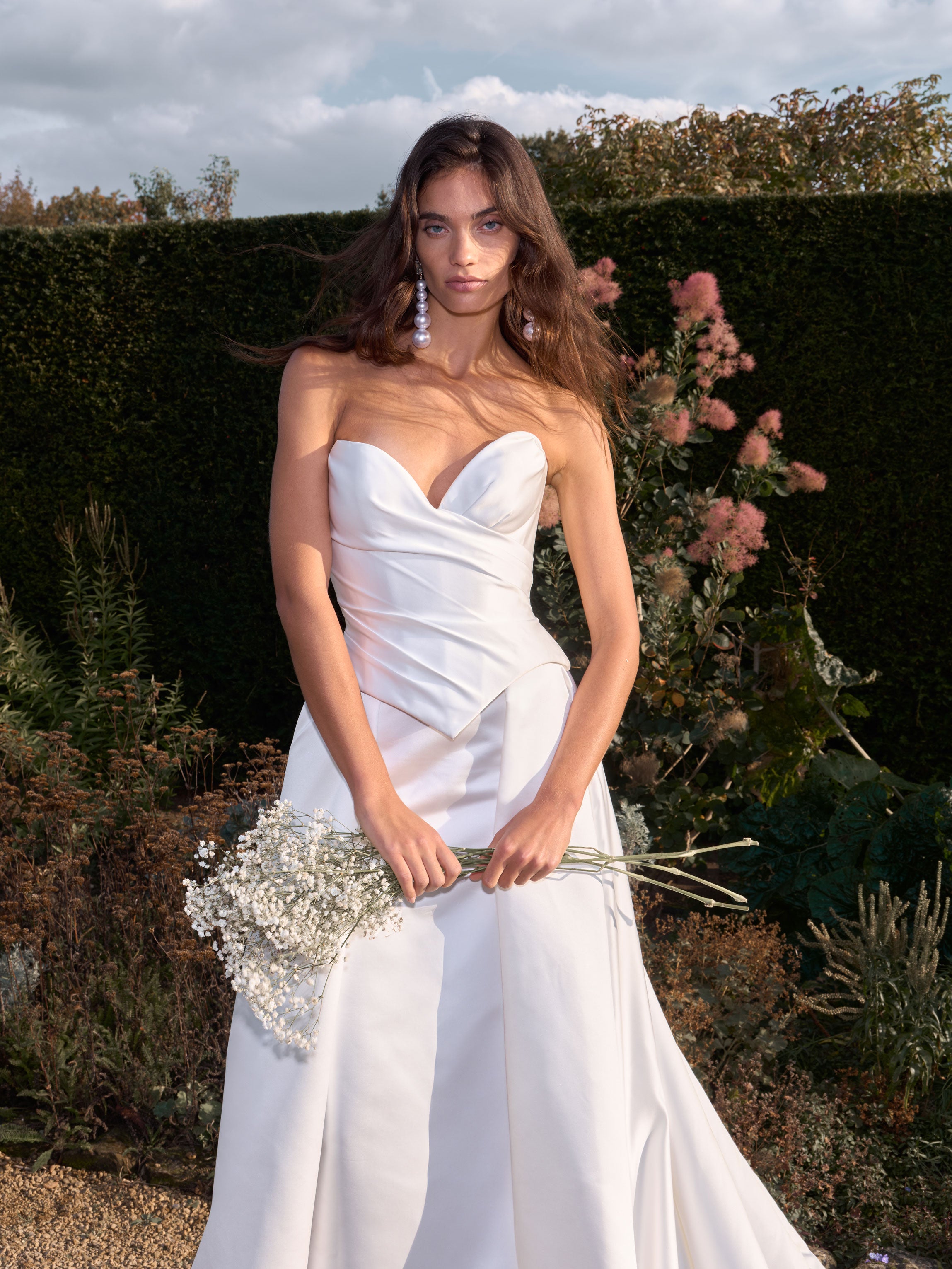 Woman in a white strapless dress holding flowers in a garden setting